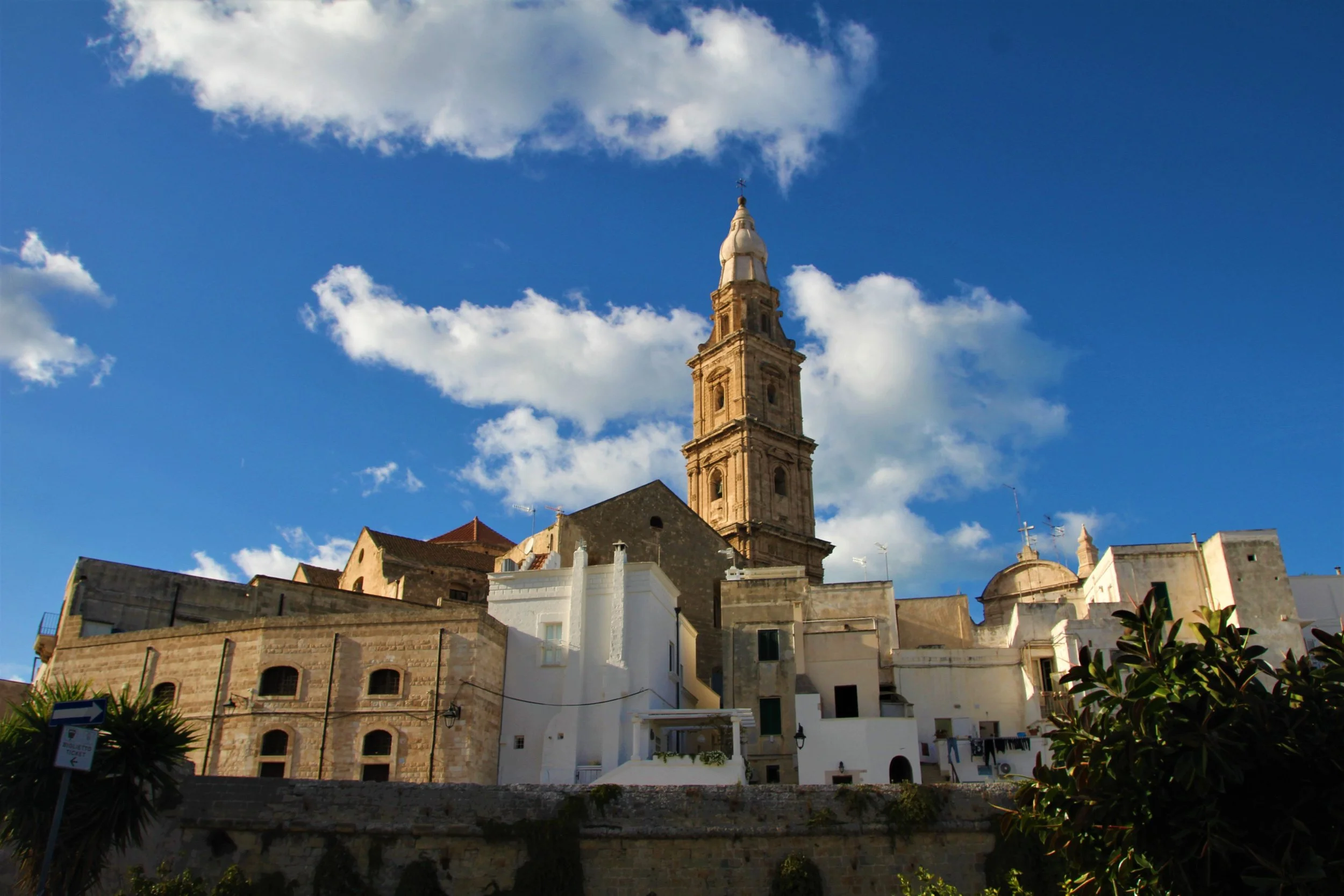 Historic church tower and whitewashed buildings in Monopoli, Puglia beneath a blue sky, showing the architecture of Southern Italy.