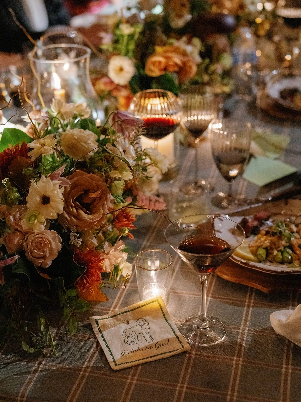 An intimate wedding tablescape featuring floral arrangements, candlelight, crystal glassware, and a cocktail napkin detail styled for a luxury reception.