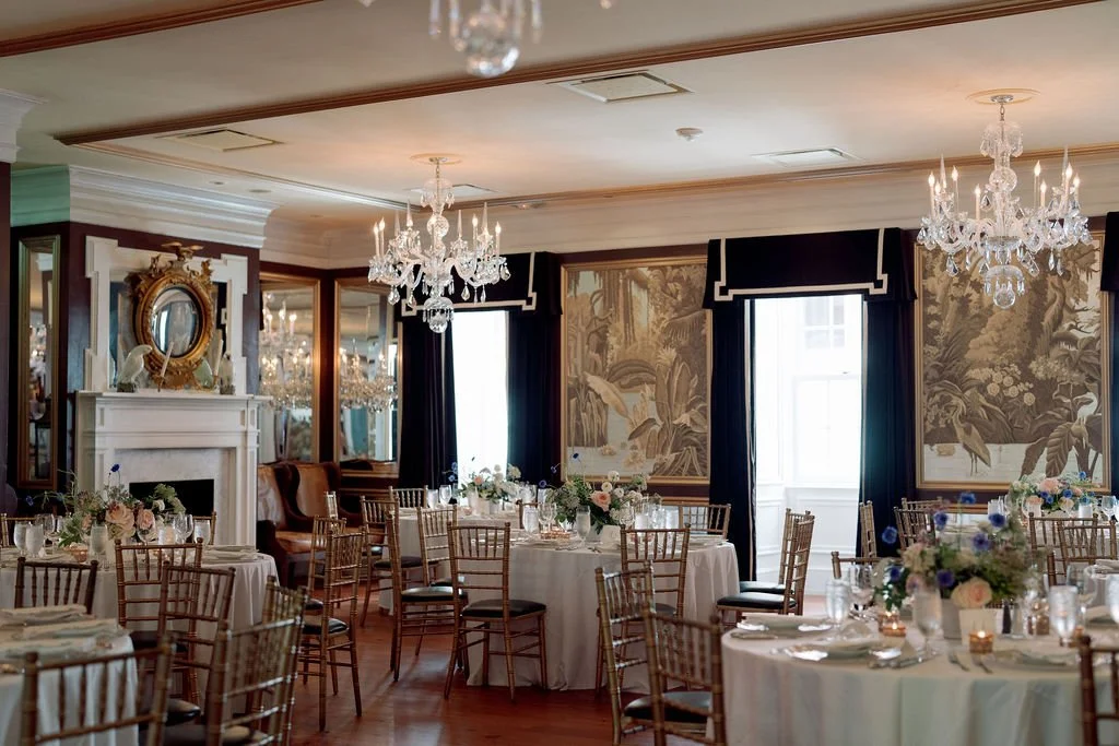 Intimate wedding reception inside a historic home with chandeliers, round dining tables, floral centerpieces, and layered architectural details.