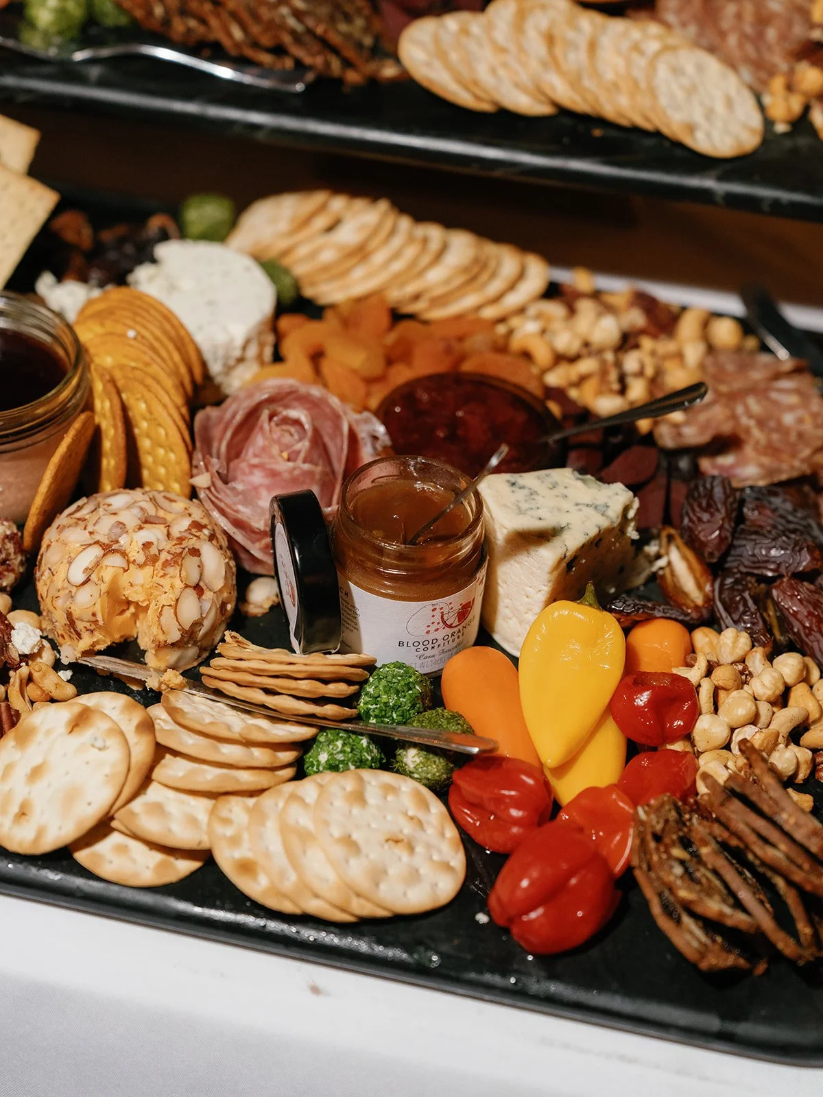 Charcuterie display with cheeses, crackers, cured meats, nuts, dried fruit, and colorful peppers at a wedding welcome party.