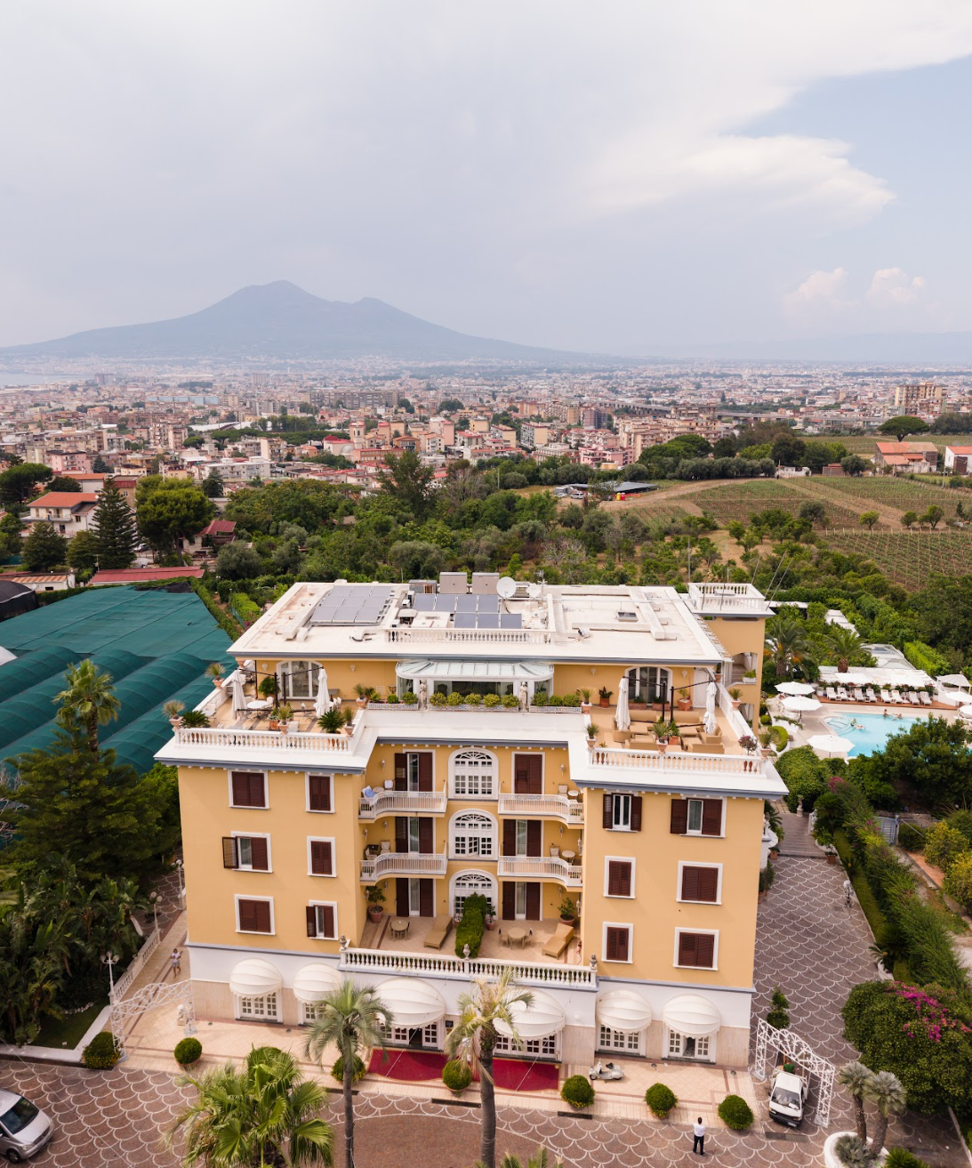 Aerial view of an Italian hotel surrounded by gardens with Mount Vesuvius in the distance.