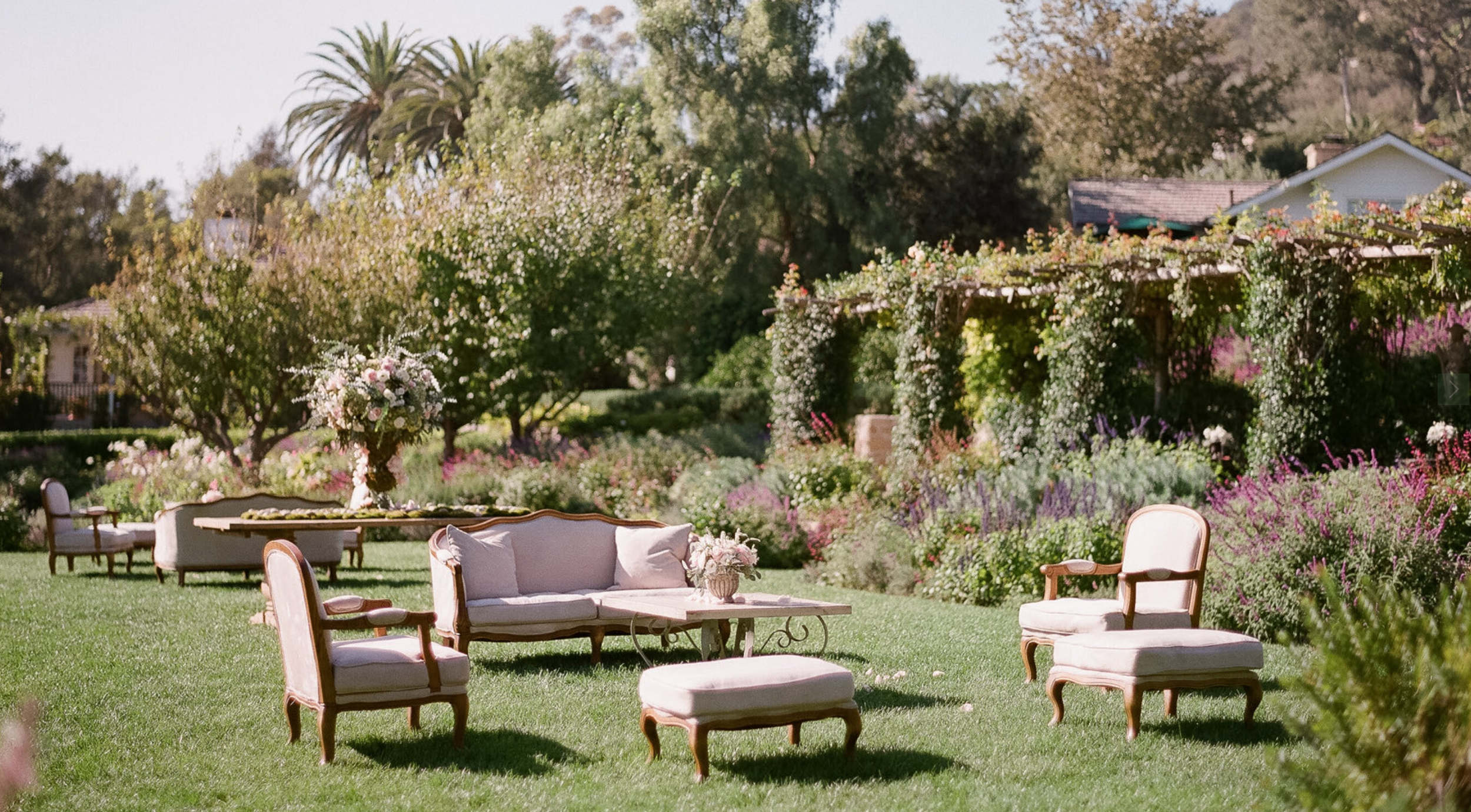 Garden lounge setup with vintage seating, florals, and a pergola backdrop at a Santa Barbara wedding estate.