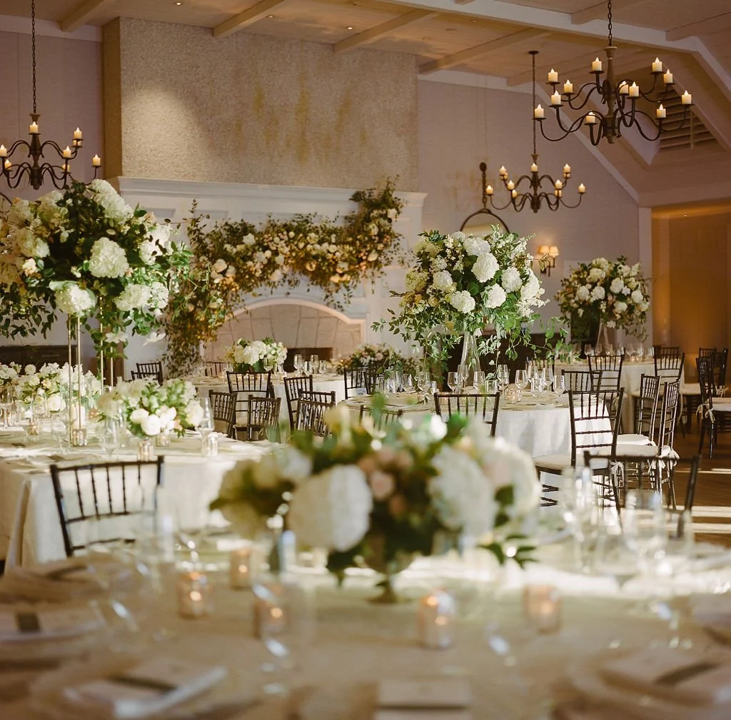 Indoor Kiawah Island wedding reception with white and green floral arrangements, candlelight, round dinner tables, and dark wood chairs.