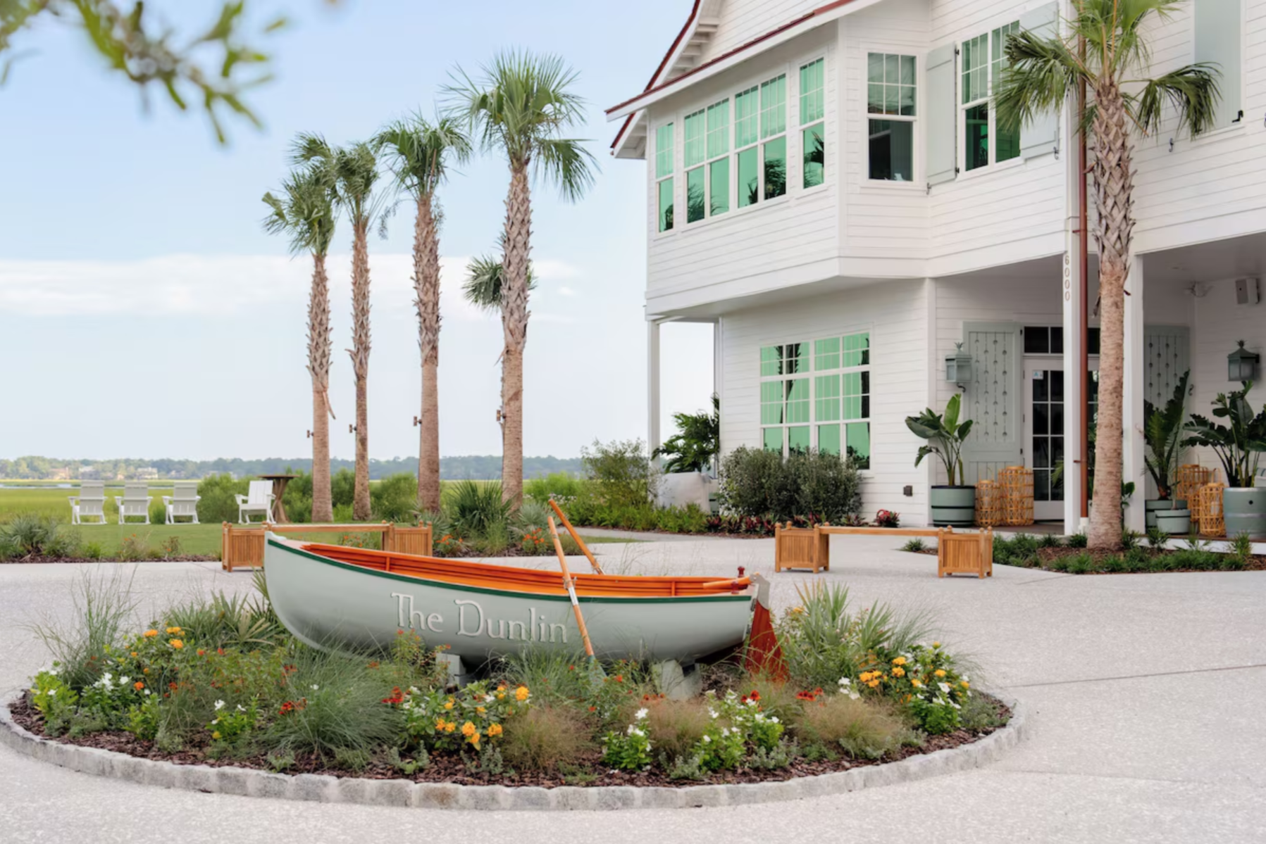 The Dunlin entrance on Johns Island with palm trees, white coastal architecture, and a rowboat display reading “The Dunlin” near the marsh.