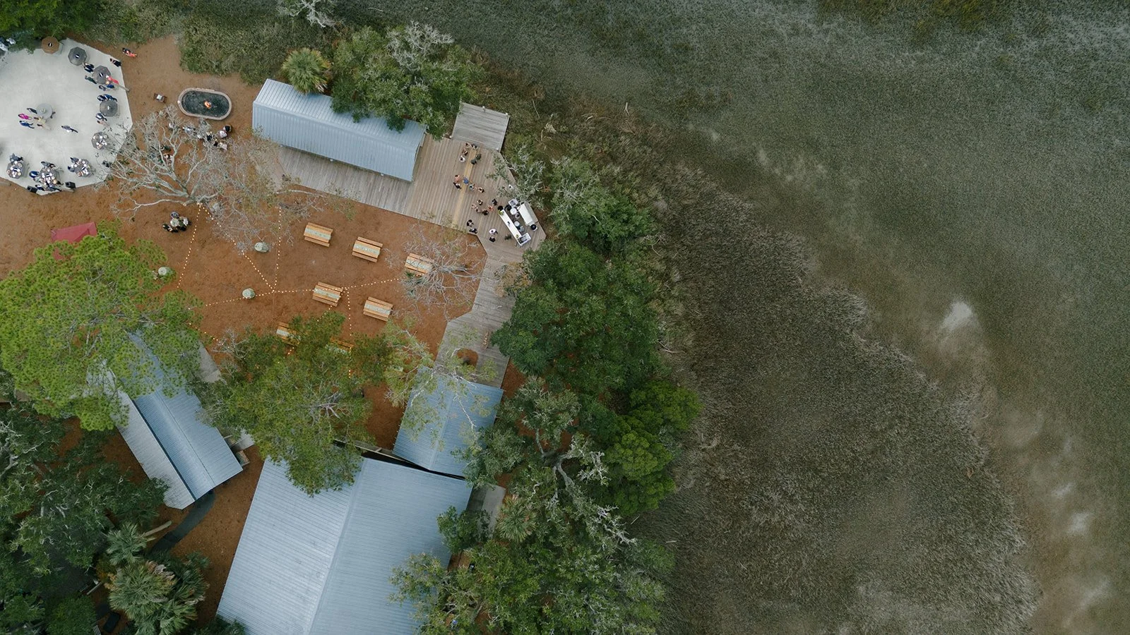 Aerial view of a welcome party at Mingo Point with outdoor gathering spaces, wooden decks, trees, and the surrounding Kiawah Island marsh.