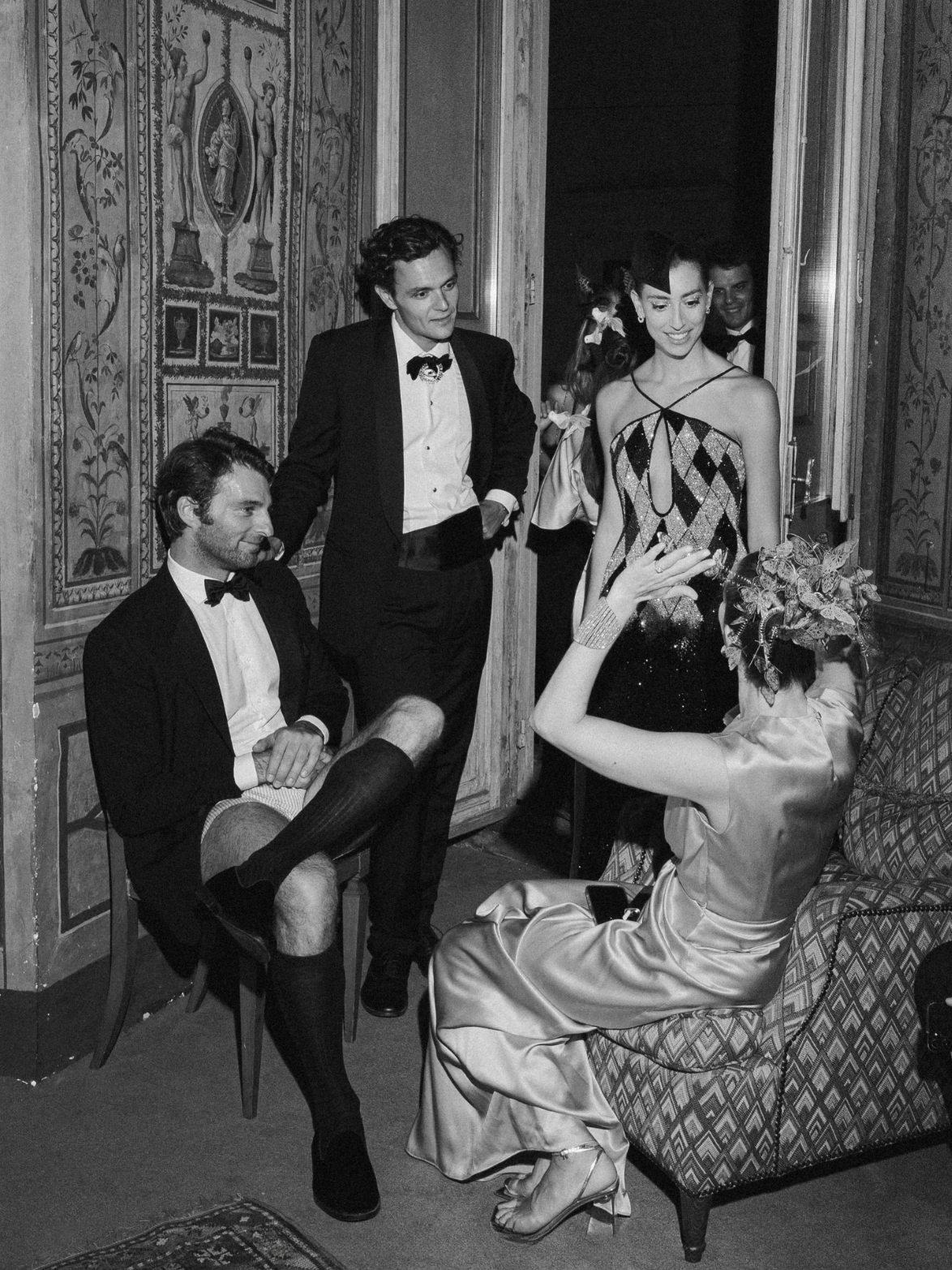 Black-and-white photograph of an elegant formal gathering with guests in evening attire, capturing a timeless sense of nostalgia, intimacy, and human connection in event design.