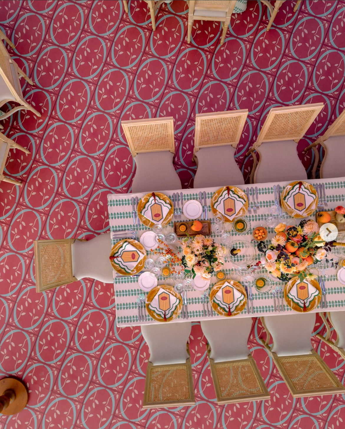 Overhead view of a richly layered wedding table with bold patterned flooring, graphic linens, sculptural place settings, and warm-toned florals, reflecting a maximalist approach to event design.
