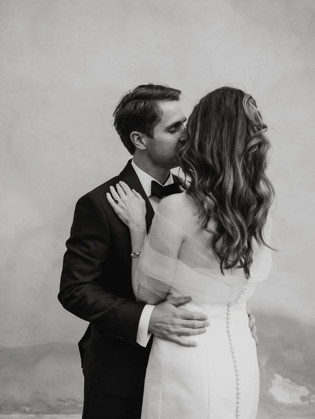 Black-and-white wedding portrait of a bride and groom sharing a kiss during their wedding celebration.