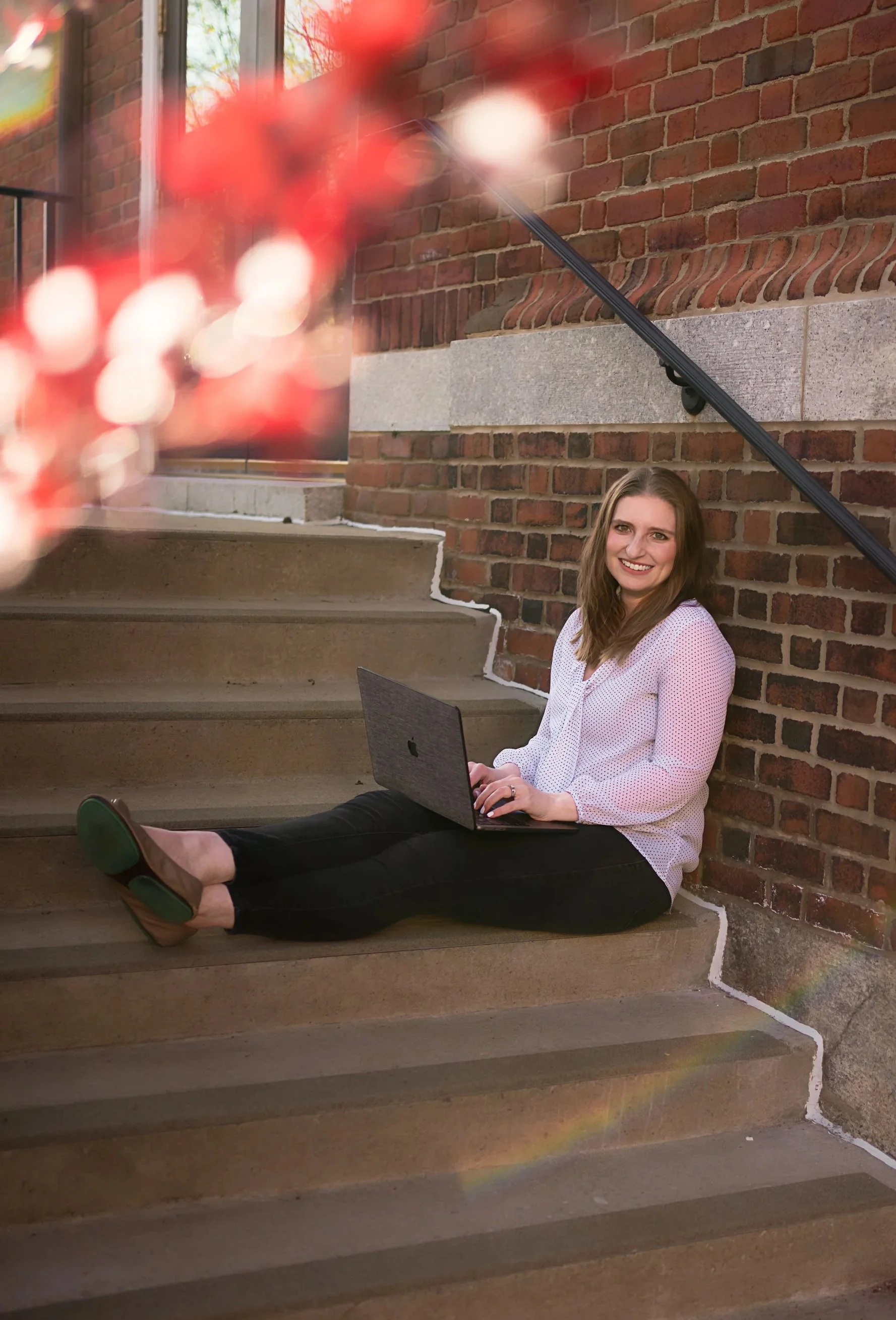 Book coach for women writers Lisa Fellinger smiling with laptop on outdoor staircase, helping novelists gain confidence and finish their books.