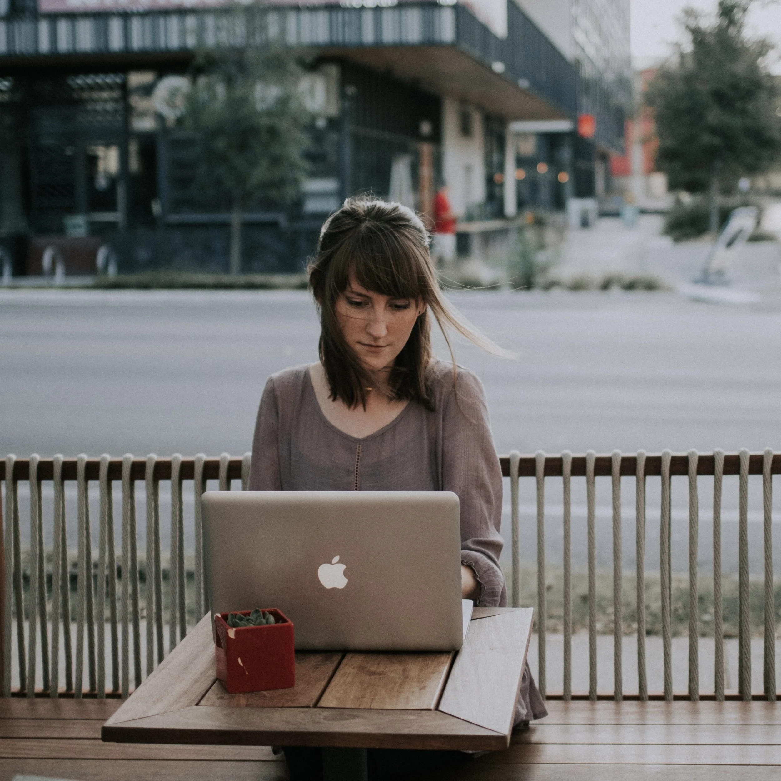 Woman sitting outside writing on her laptop, representing book coaching for novelists who want guidance, accountability, and support to finish their novels.
