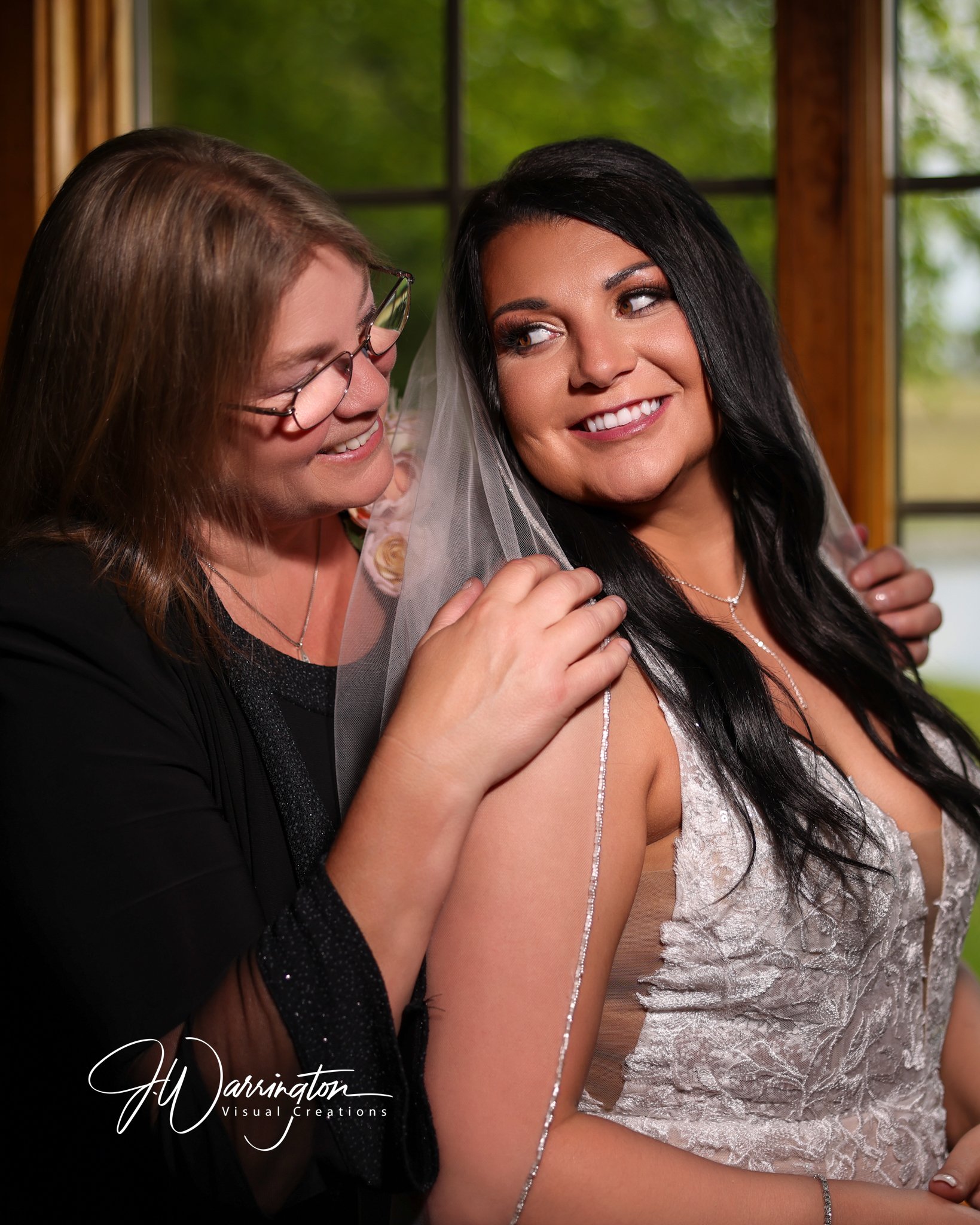 Wedding day moment of a mother helping  bride daughter adjust her bridal veil in front of a window photography by J. Warrington Visual Creations in Findlay, Ohio.