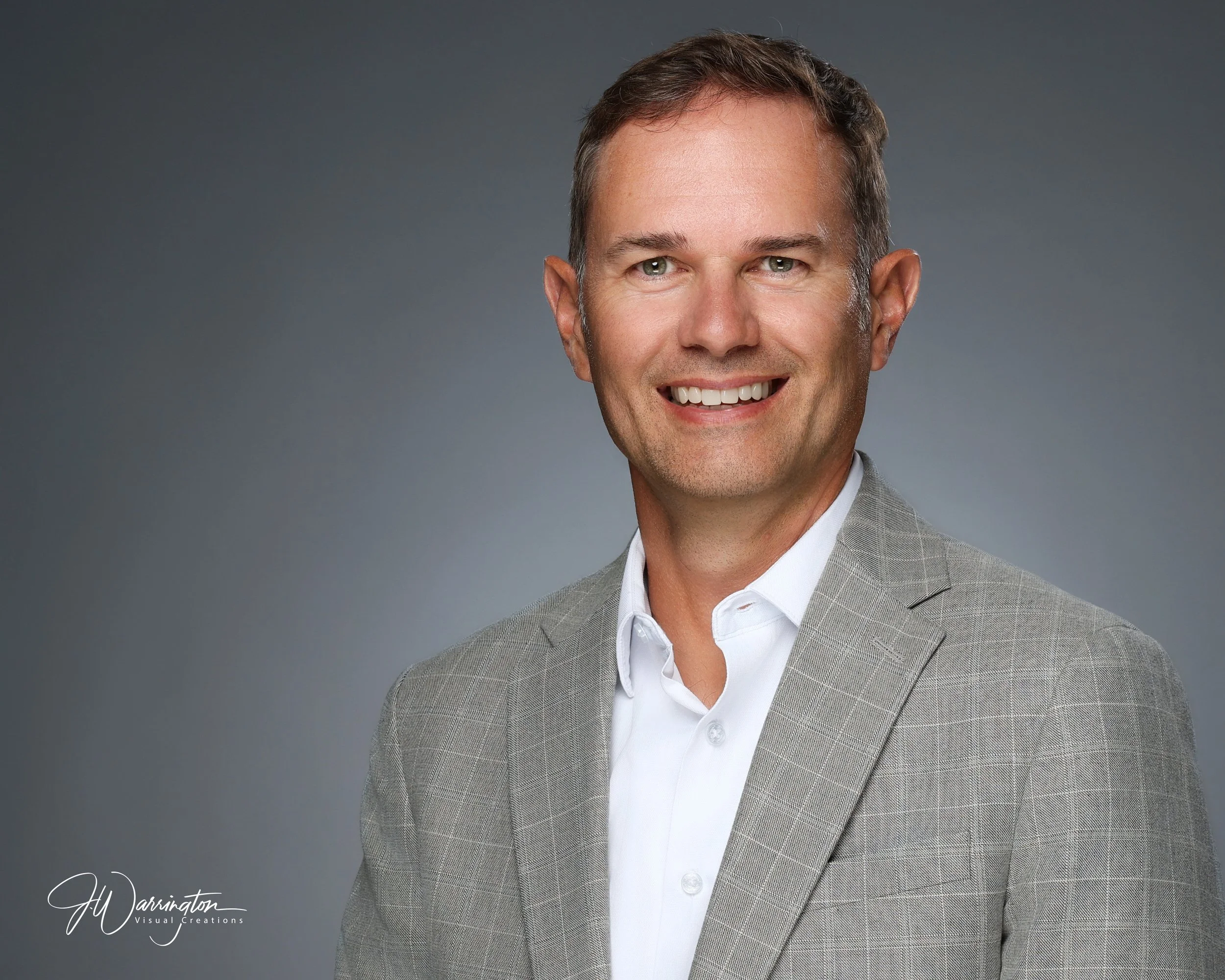 Professional corporate headshot of a smiling businessman wearing a gray windowpane jacket by northwest ohio photographer 