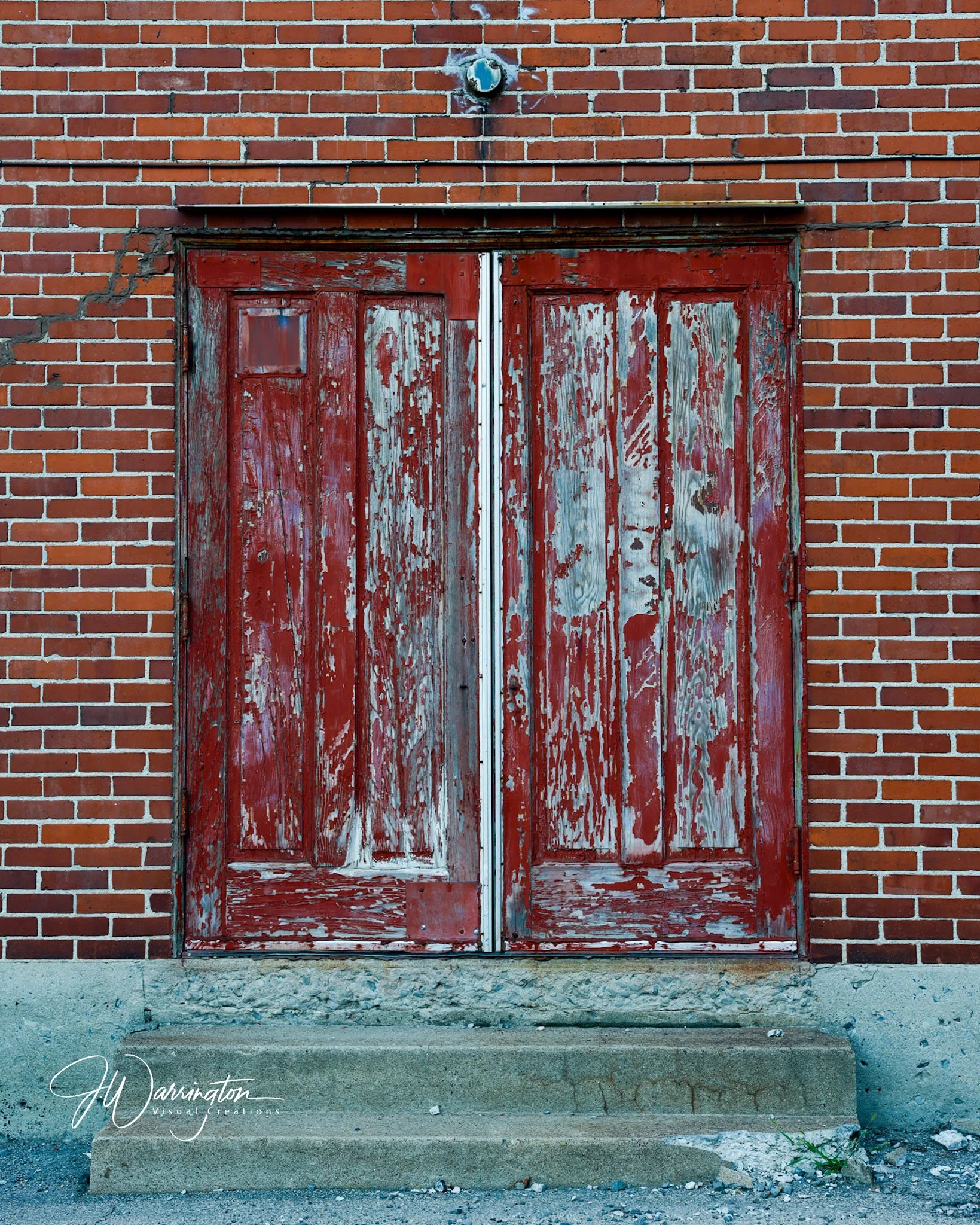 A brick wall in Downtown Lima, with an old, weathered, red wooden door set into it. The door has peeling paint and a small window at the top. A metal strip runs vertically in the middle of the door, and there's a concrete step at its base.