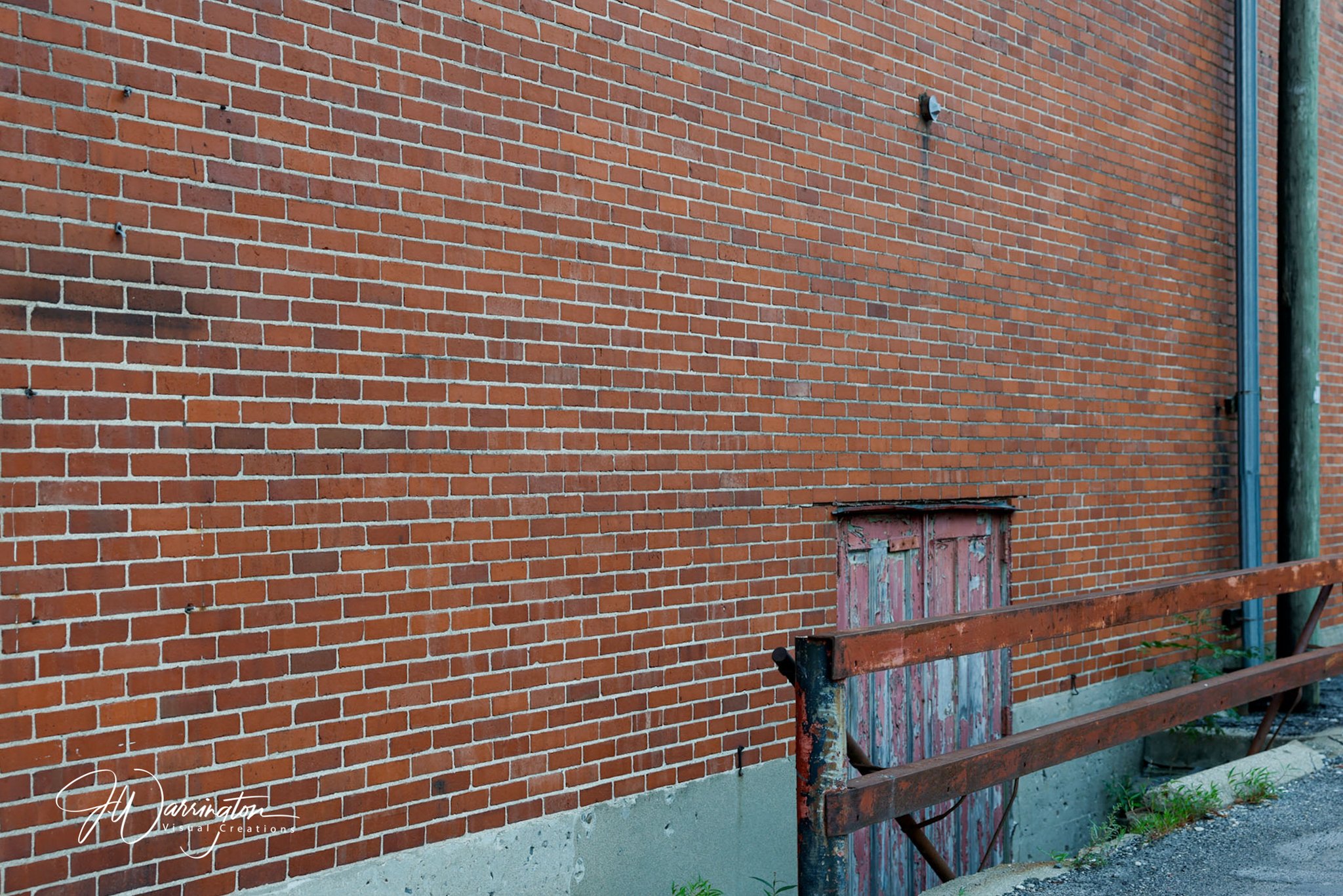 Close-up of a brick wall with metal hooks and a small, weathered wooden door beneath the wall, with a metal railing in front, Downtown Lima.