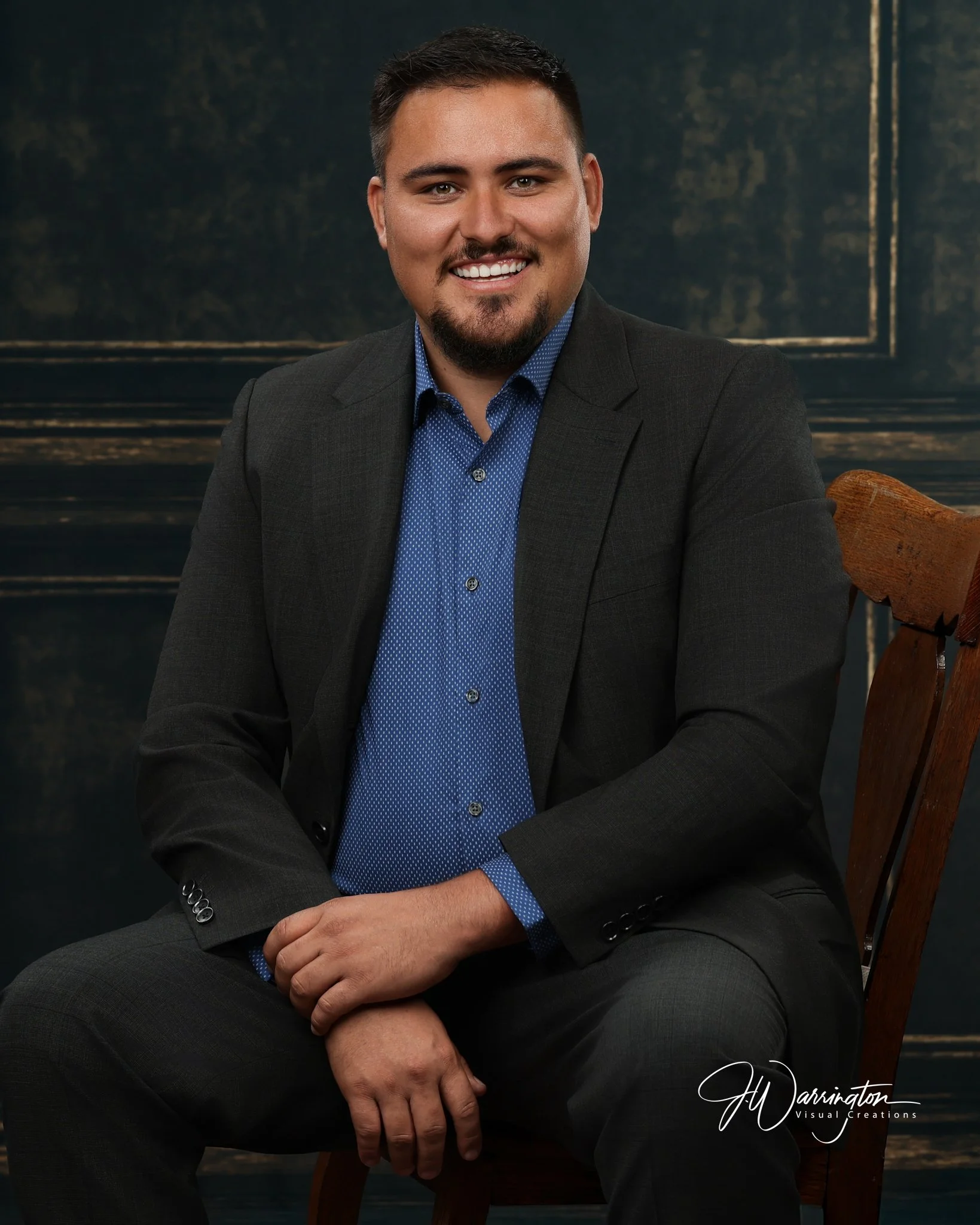 Executive branding headshot, dark jacket, blue shirt, on a green paneled wall.