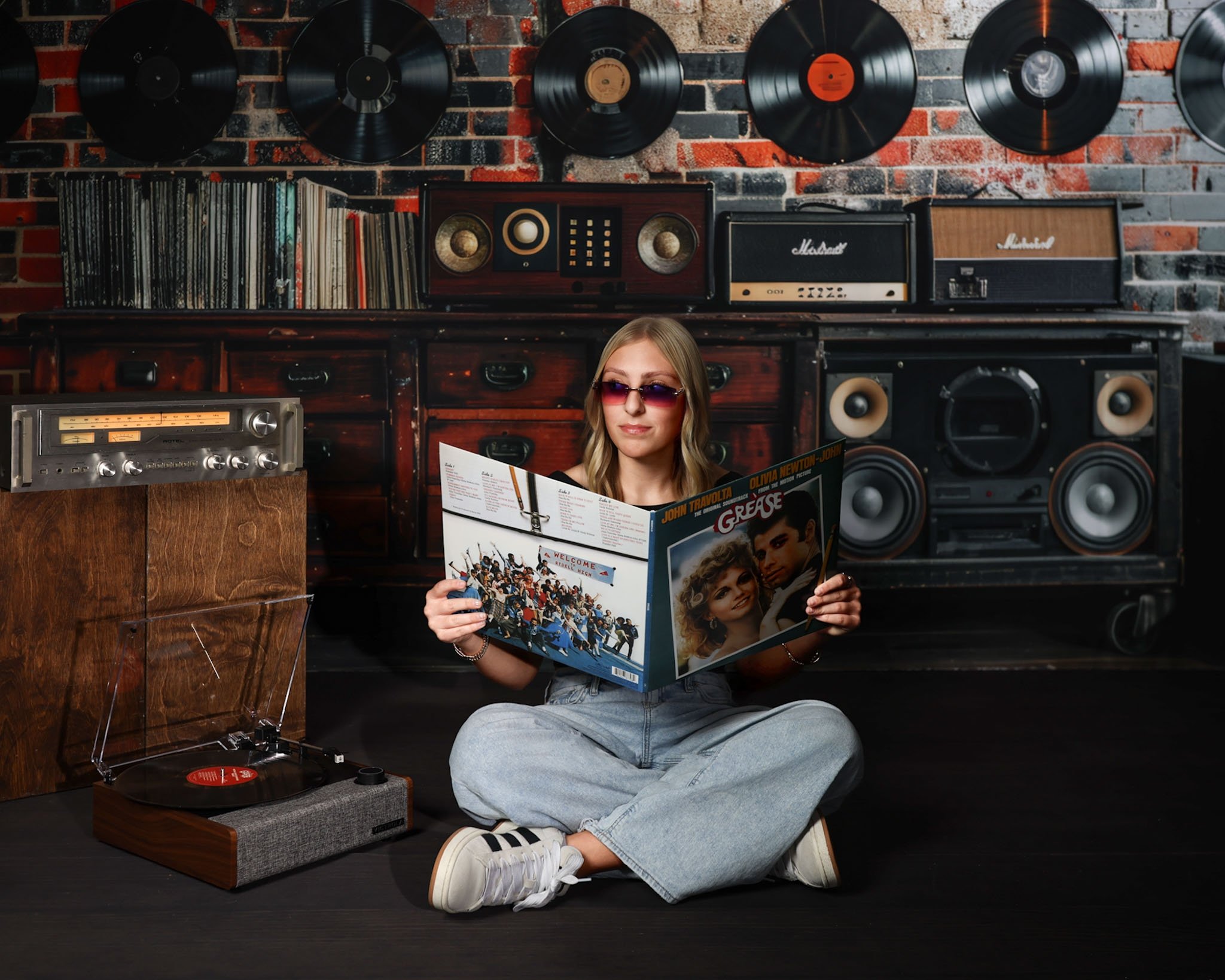 Creative retro studio portrait of a cool teenage girl sitting on the floor reading a record album, surrounded by vintage vinyl and audio equipment, captured by northwest ohio photographer