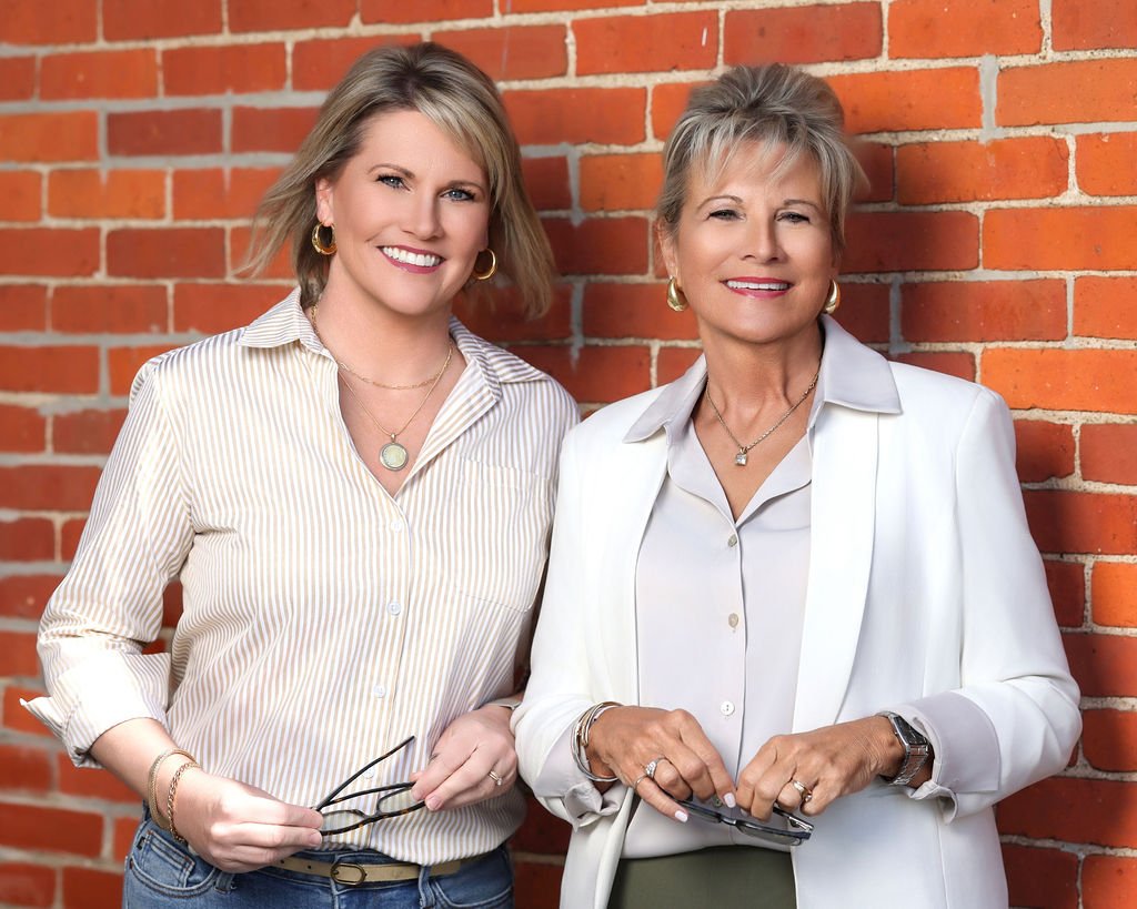 Two female professionals during a photoshoot outside an exposed red brick wall