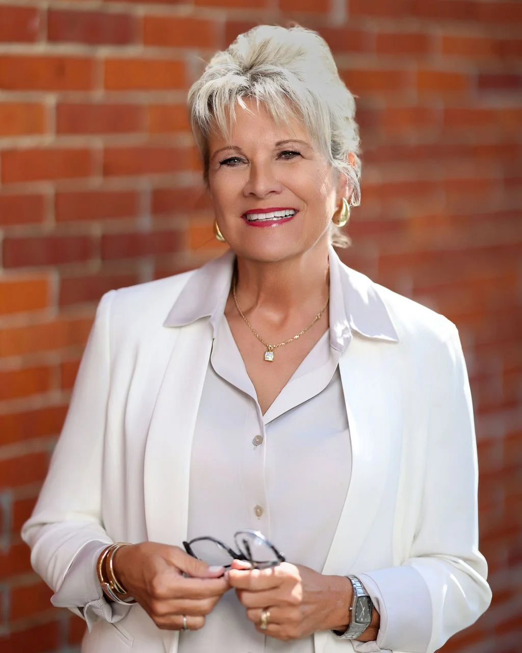 Professional business headshot of a female professional in a white blazer against a red brick backdrop 