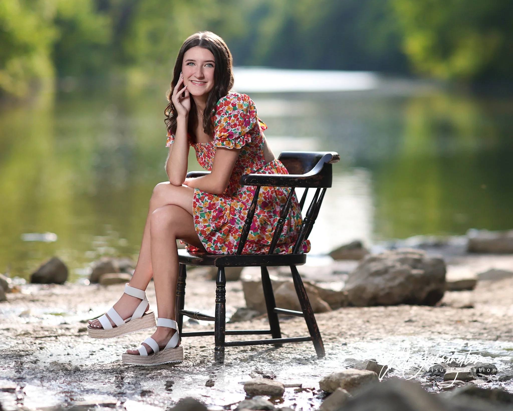 Woman in floral dress sitting in a chair by the river outdoors with blurred green background at Riverside Park.