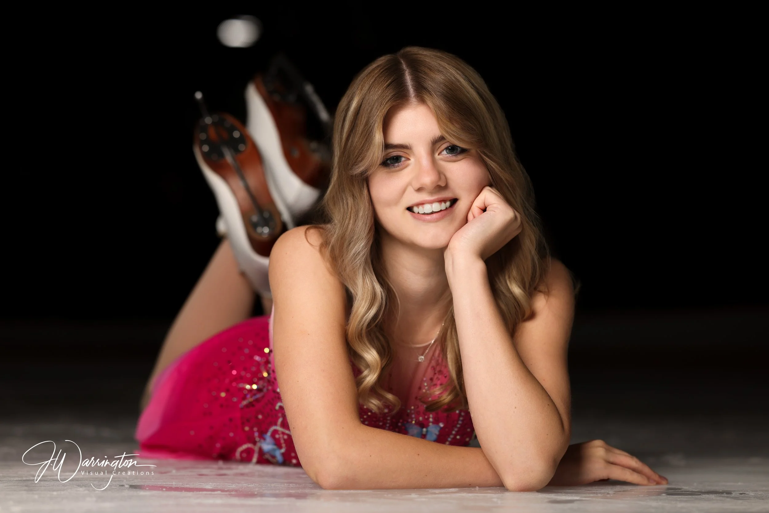 Female senior figure skater, smiling and laying on the ice.