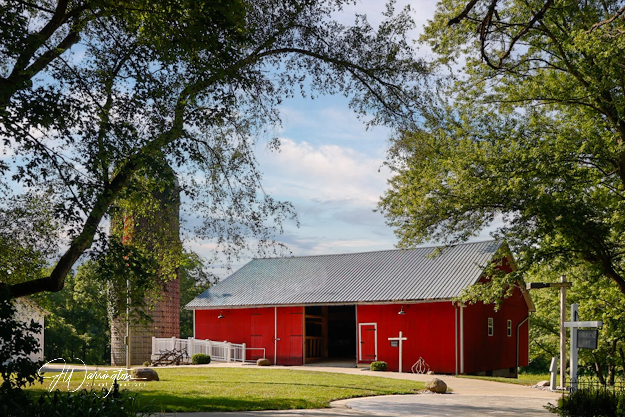 A red barn with a gray roof surrounded by green trees and a landscaped lawn at Lauer Historical Farm.