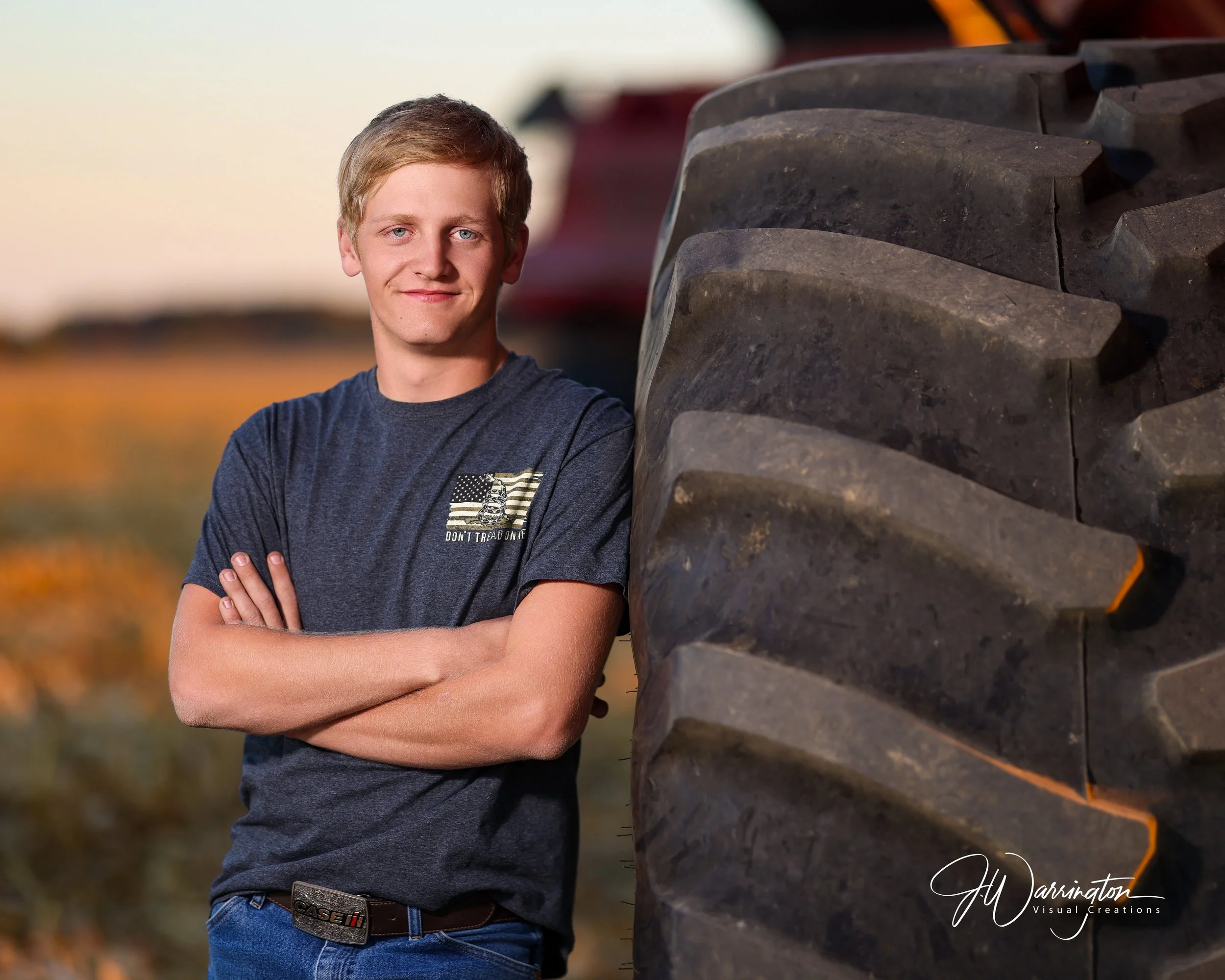 Male senior leaning against a large tractor tire.