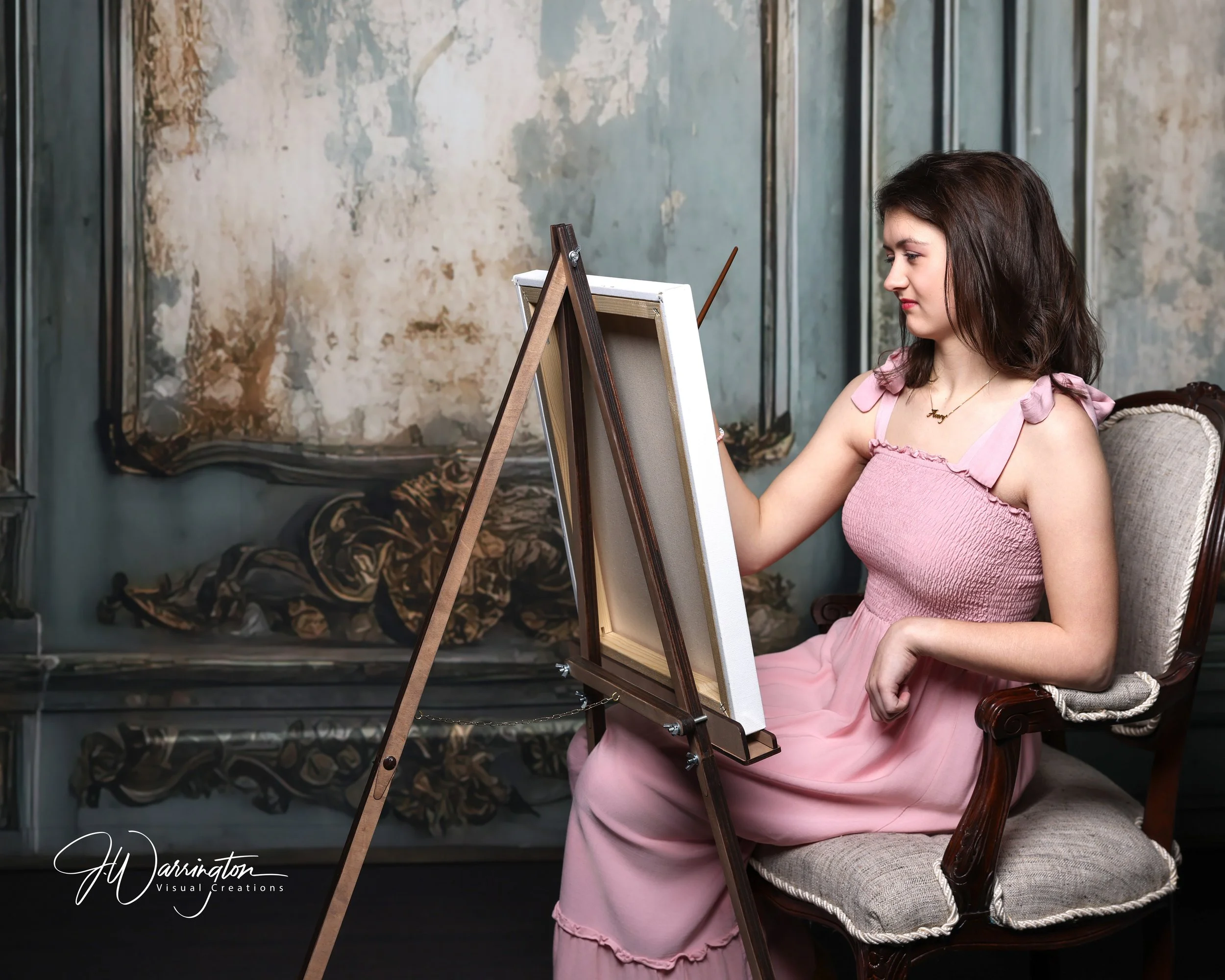 Young lady in a pink dress painting on a canvas in front of distressed backdrop