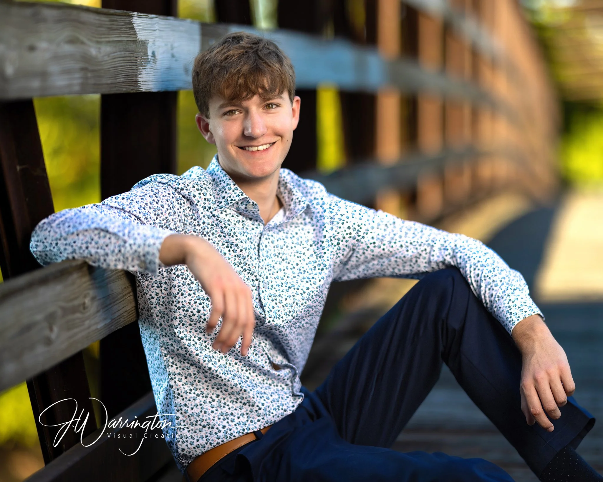 Young man posing comfortably outside on a bridge with one hand resting on his knee