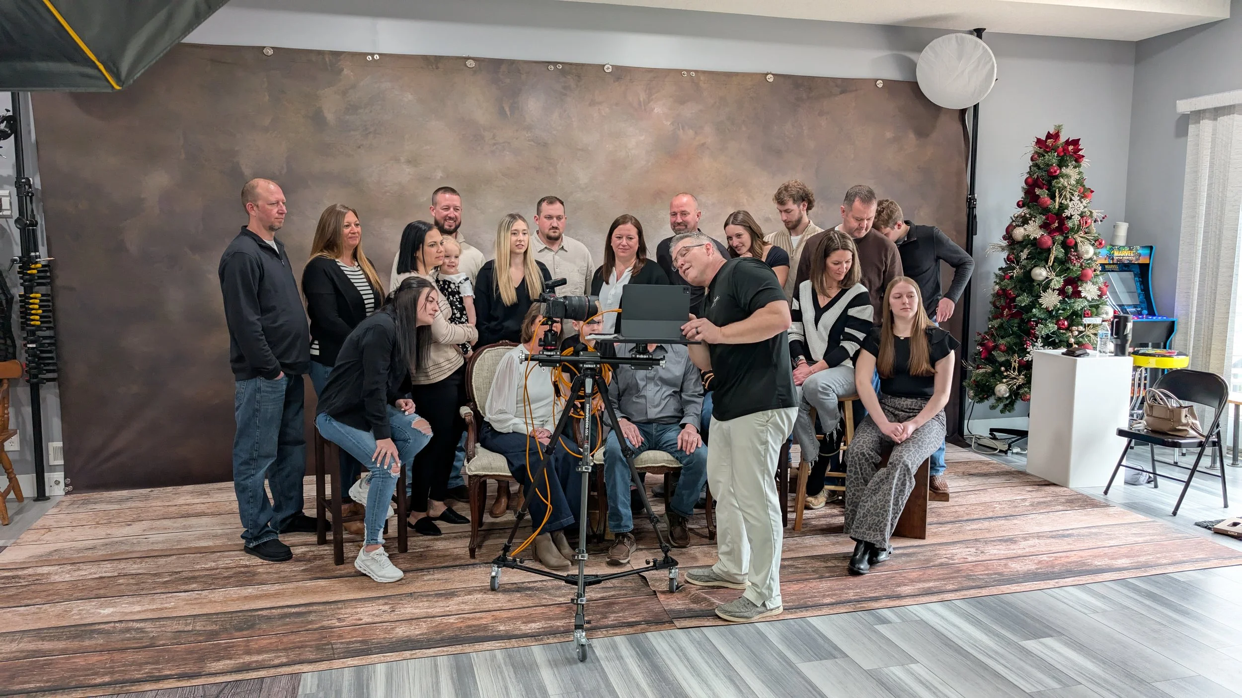 A group of people posing for a photo in a studio with a Christmas tree on the right side and a photographer taking their picture.