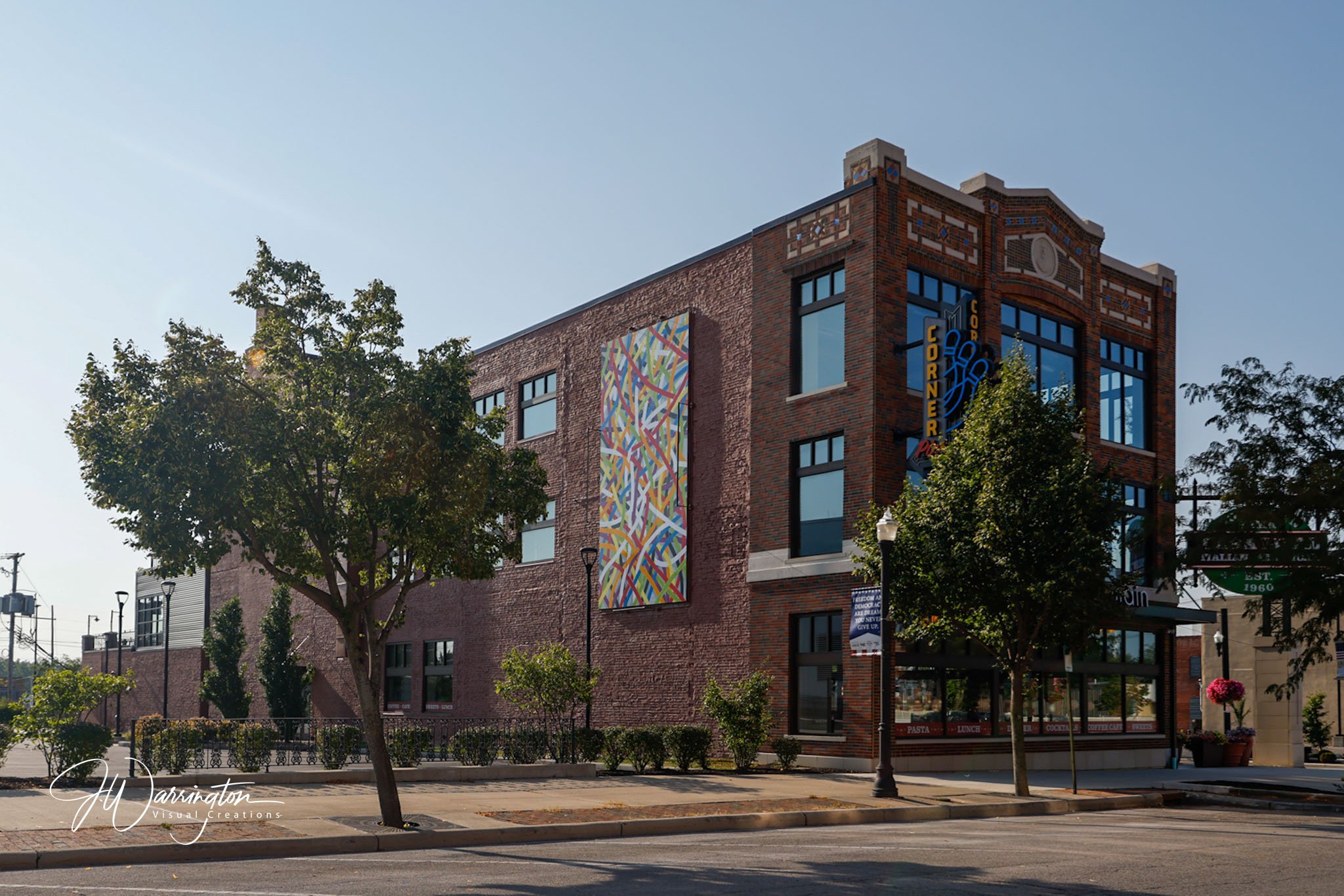 A brick building in Downtown Lima with large windows and colorful artwork on the wall, surrounded by trees and streetlamps under a clear blue sky.
