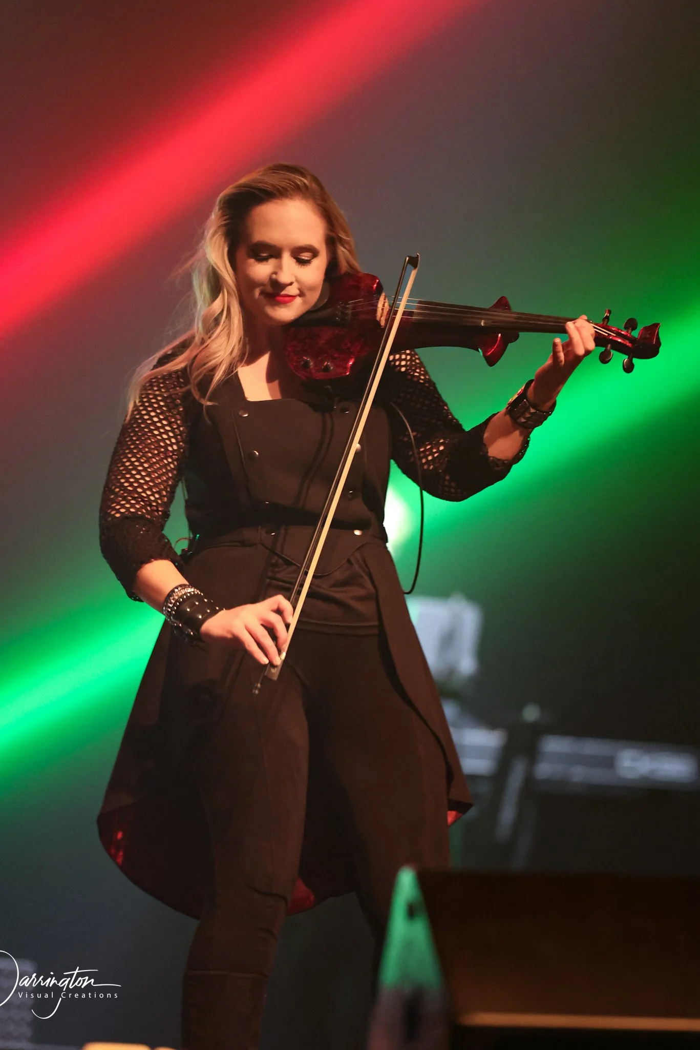 A female violinist performs on stage under vibrant green concert lighting captured by Northwest Ohio photographer
