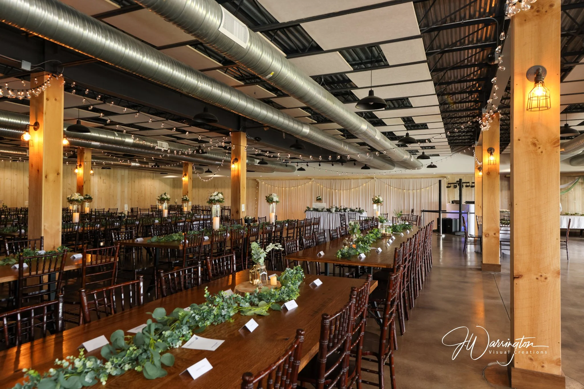 Indoor wedding reception venue with long wooden banquet tables, elegant greenery garlands, and romantic string lights, captured by northwest ohio photographer 