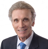 Portrait of an older man in a suit and tie, smiling against a white background.
