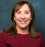 A woman with shoulder-length brown hair, wearing a maroon top, smiling against a teal background.