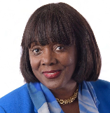 A woman with dark hair wearing a blue blazer and gold necklace, smiling at the camera.