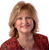 Portrait of a smiling woman with blonde hair wearing a red patterned blazer.