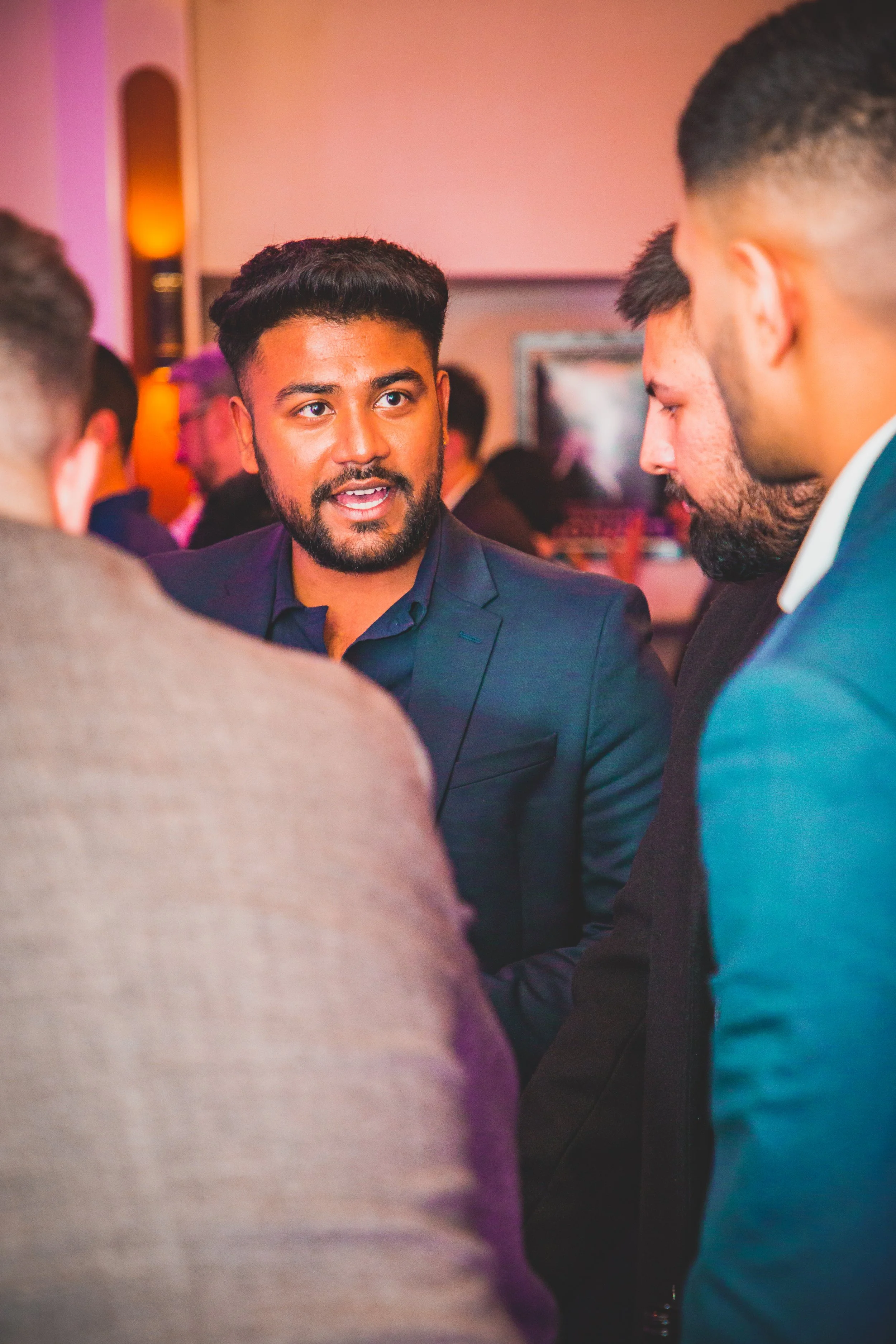 A group of men are engaged in conversation at an indoor event with warm lighting.