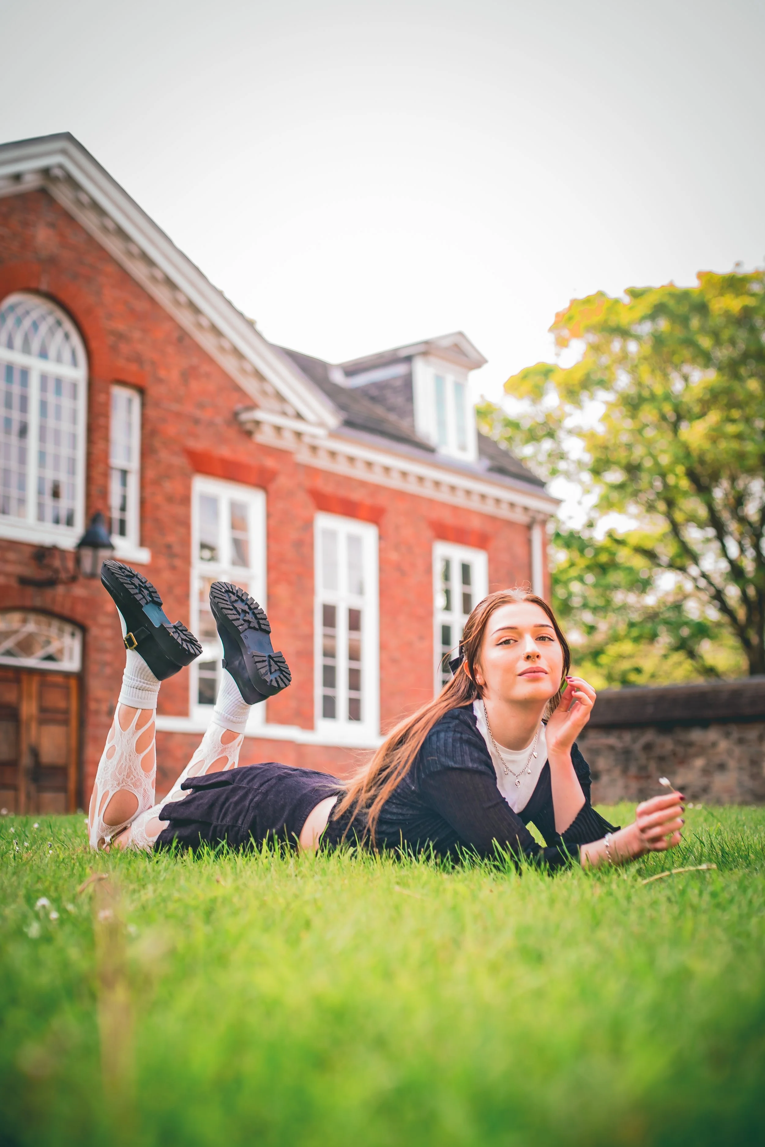 Young woman lying on grass in front of brick house, with woman lying on grass with feet raised, outside on a sunny day.