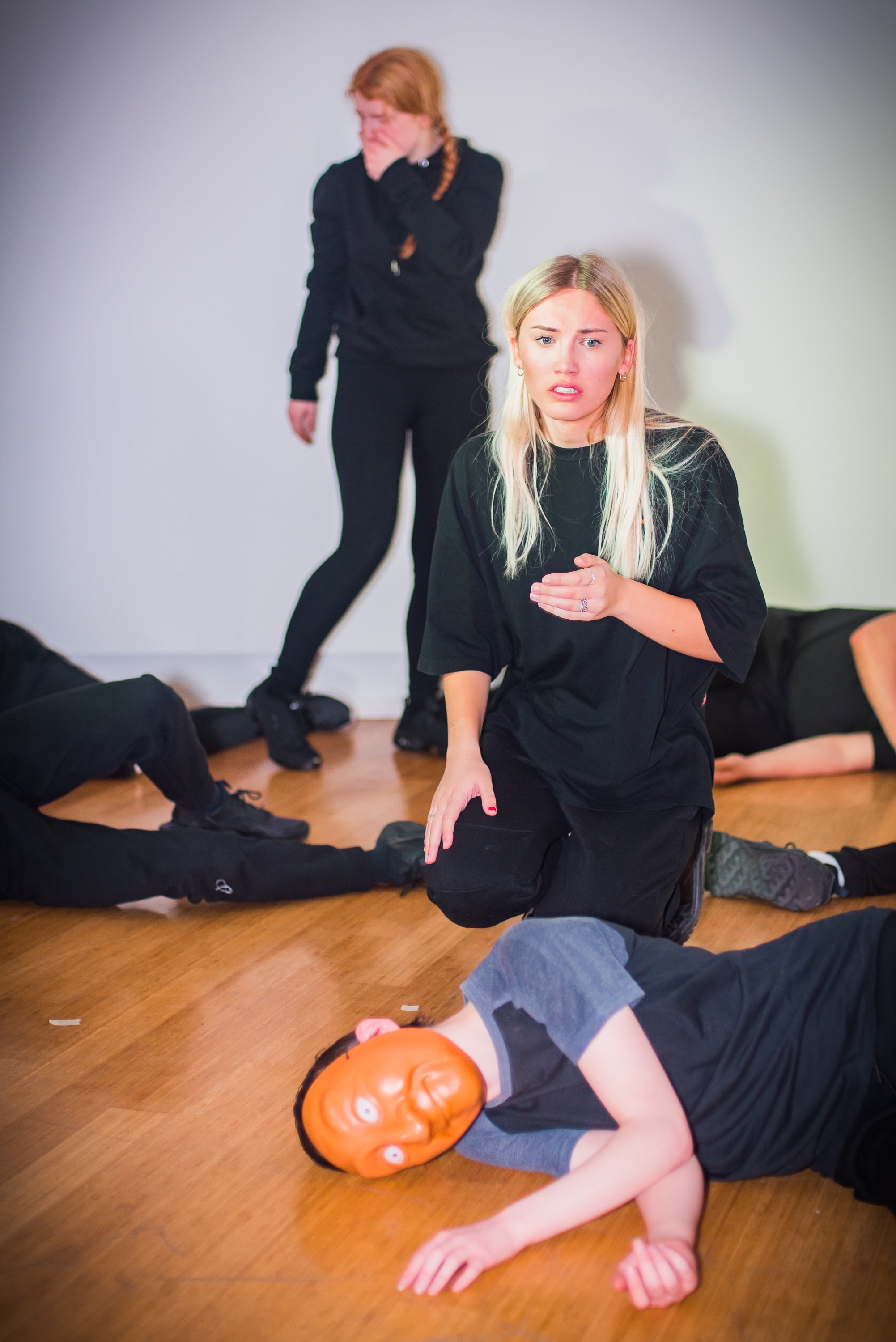 People wearing black clothing practicing a staged hostage or crime scene scenario with a mask of a clown face on the floor.