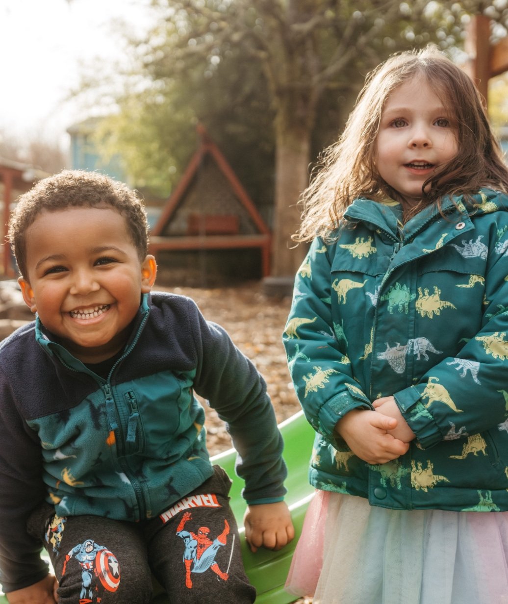 Smiling boy and girl playing outdoors in a backyard with trees and a playhouse in the background.