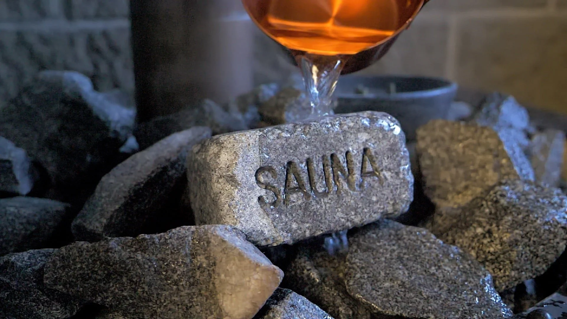 Three people sitting in a sauna, two women and one man, wearing towels and swimwear, enjoying the experience.