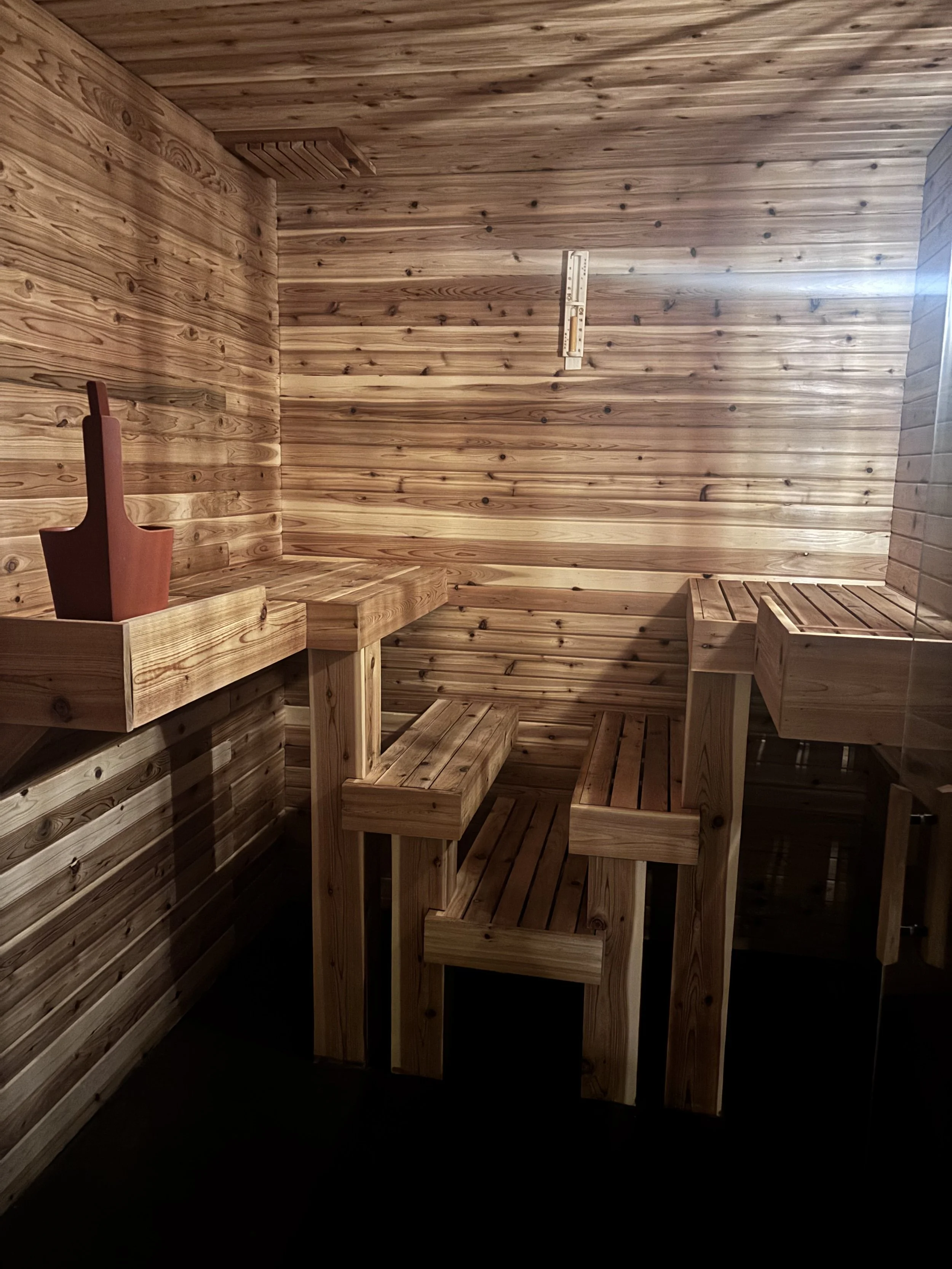 A private cedar sauna room with benches on the sides and a thermometer mounted on the wall.