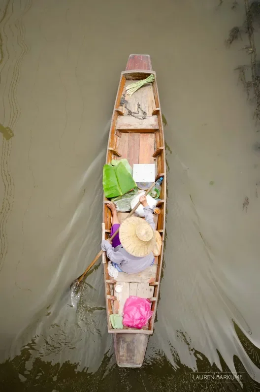 A woman in a traditional boat rows down the canals of the Damnoen Saduak floating market