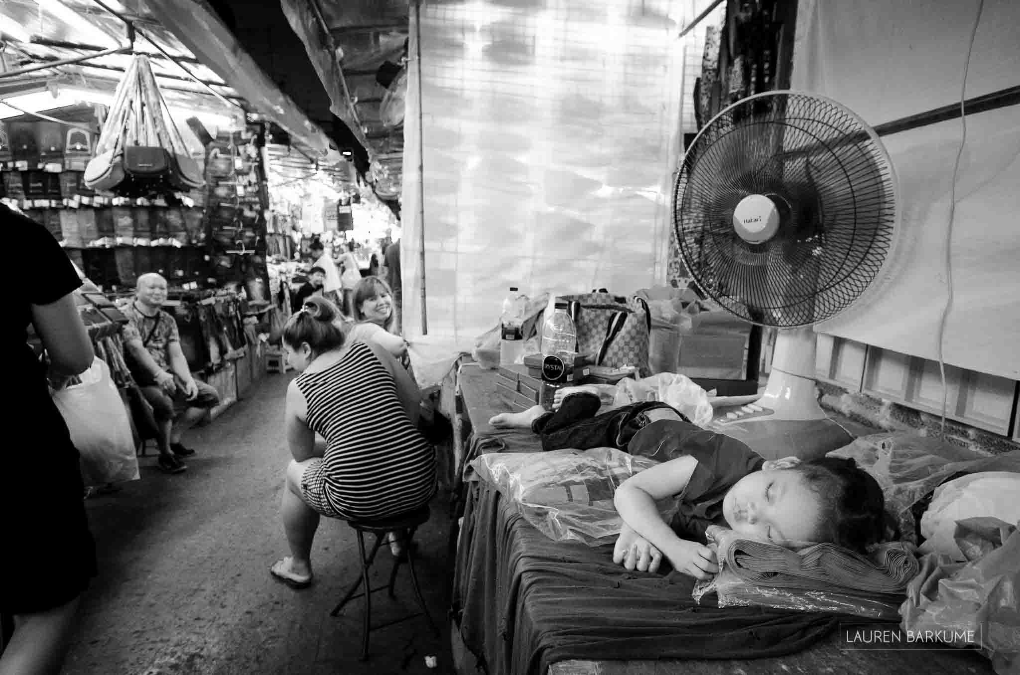 A little girl sleeps next to a fan in the Silom night market in Bangkok