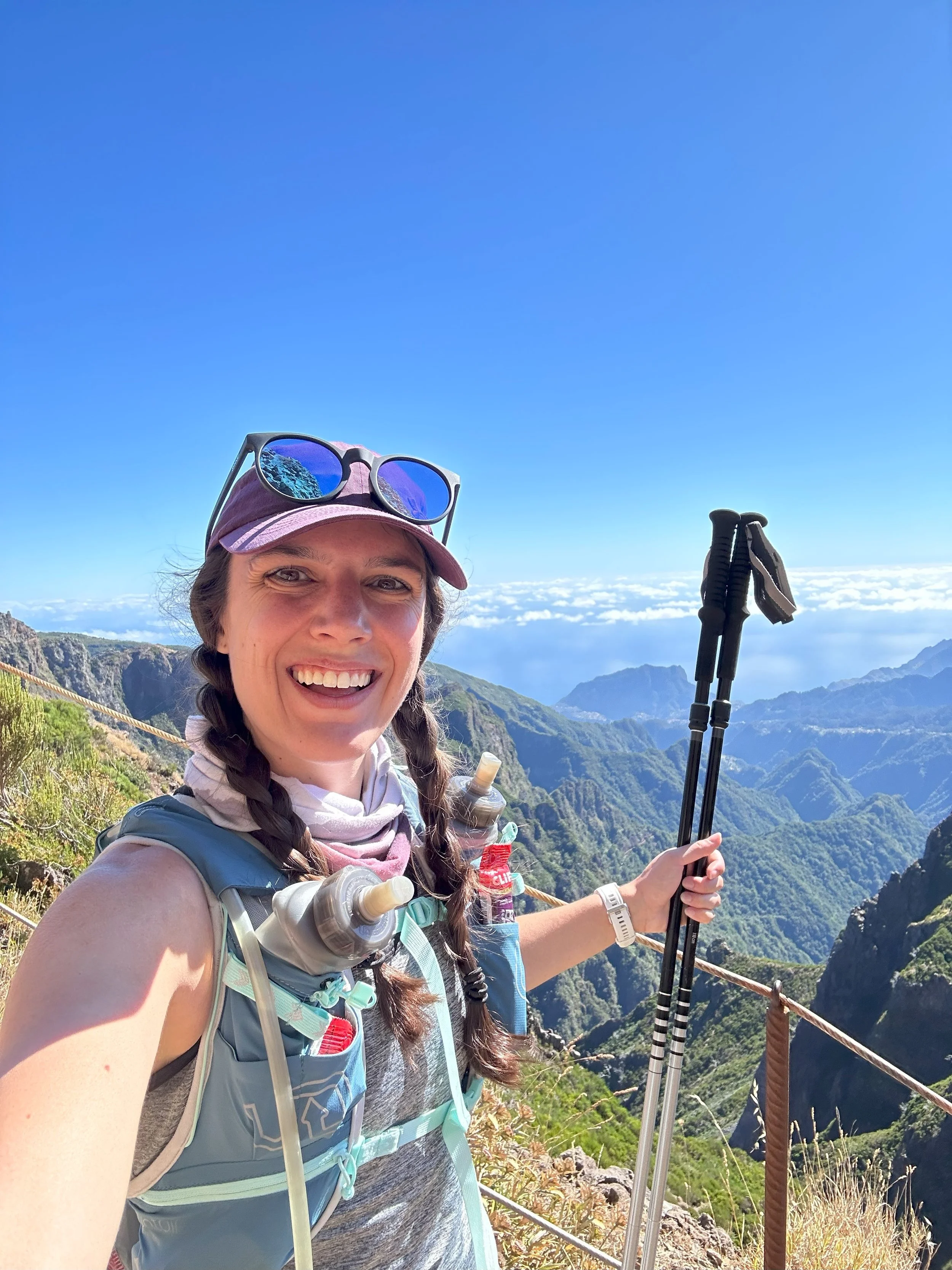 Katharine Moustakes taking selfie while trail running and holding trekking pole in left hand.