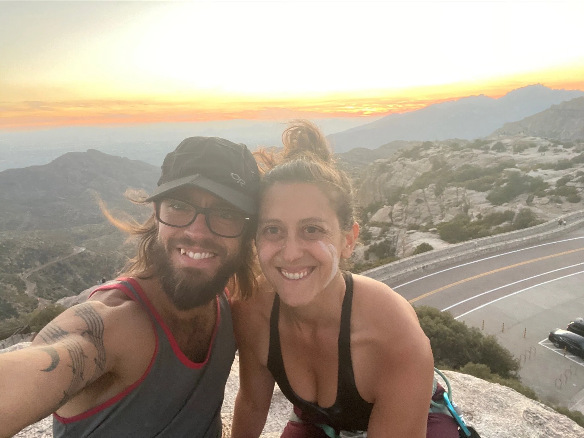 Jessica Ghantous on the right and parter on the left, taking a selfie after climbing. View of mountains in background.