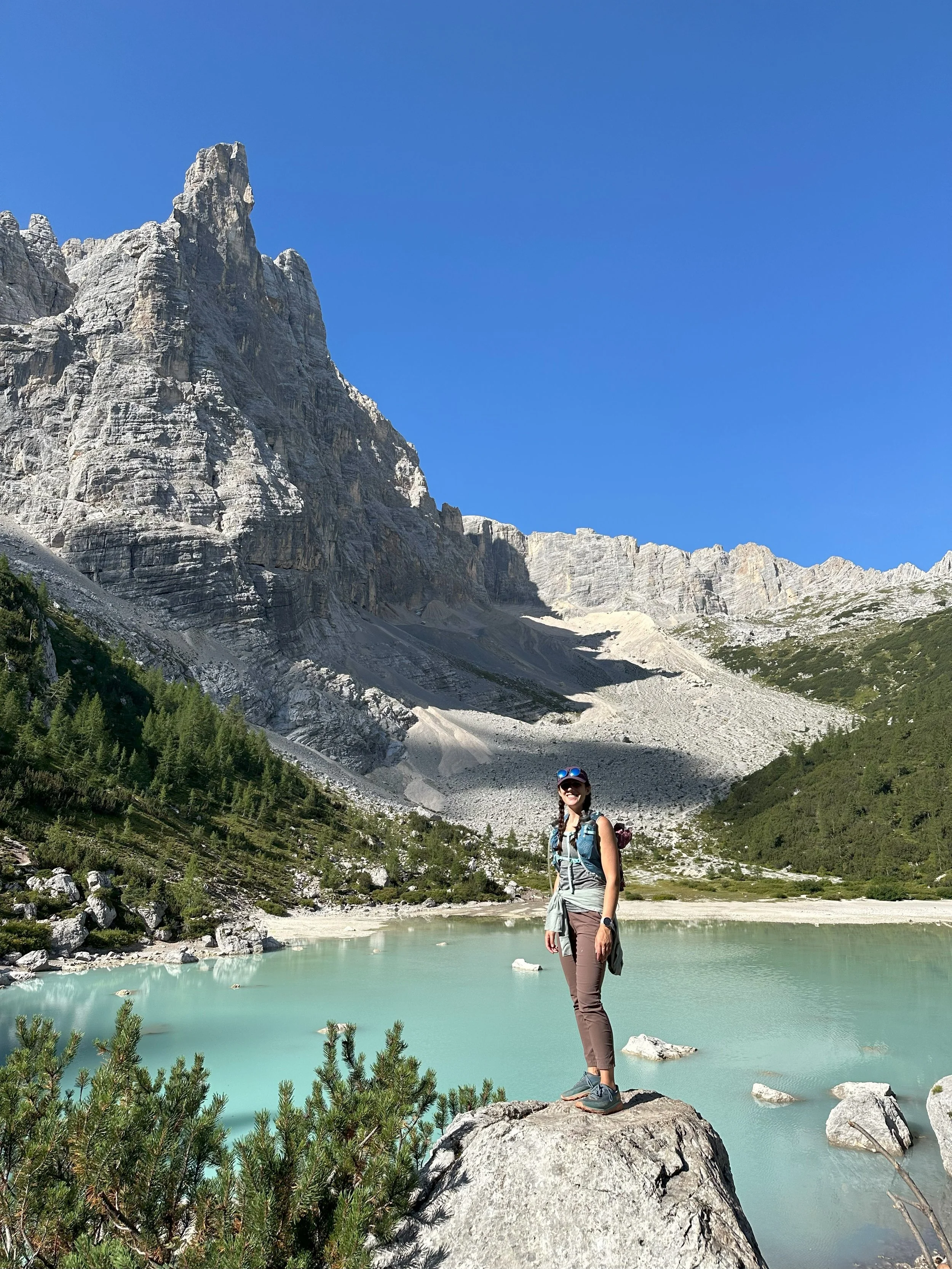 Katharine Moustakes in front of alpine lake and rocky mountain behind her.