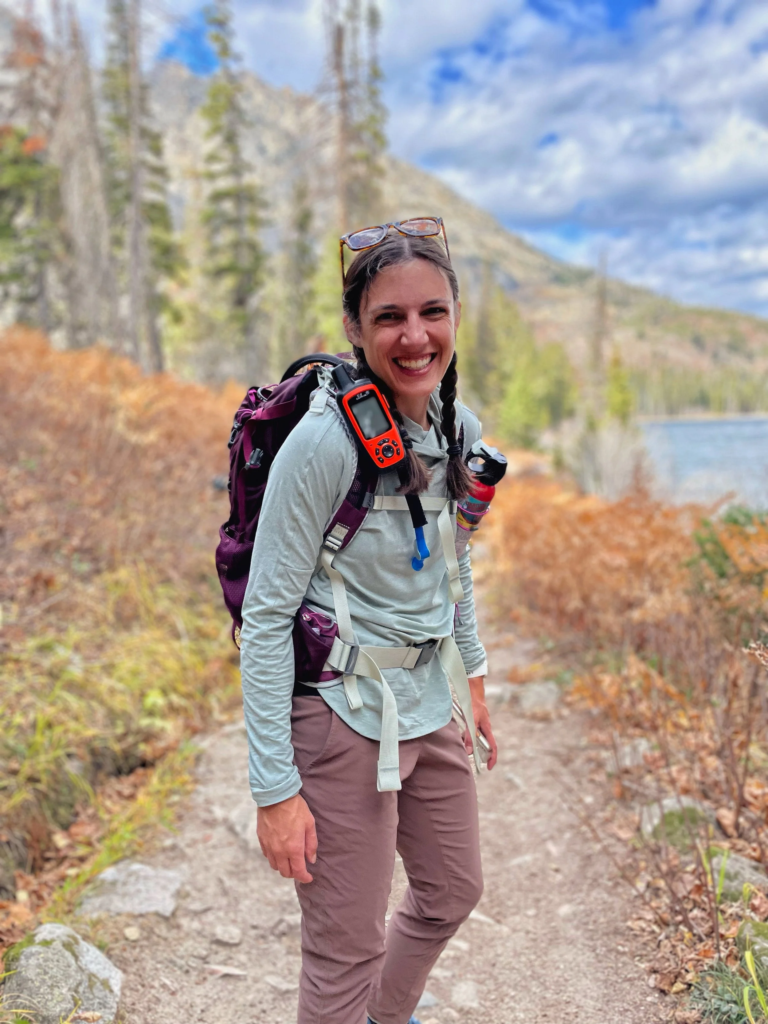 Katharine Moustakes with hair braided in pigtails and on hiking trail with backpack on.