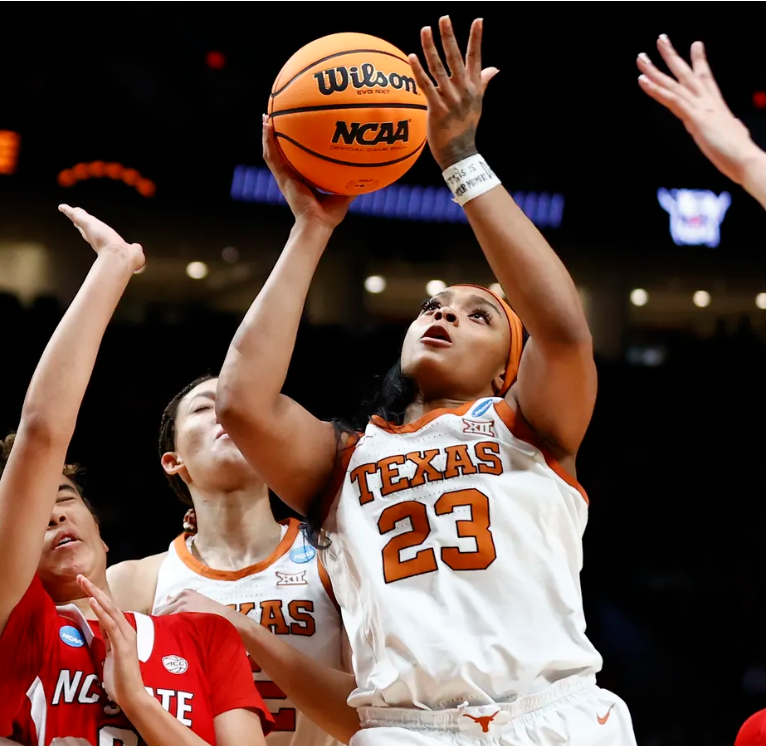 A female basketball player from Texas wearing jersey number 23 is about to make a shot during a game. Other players are around her in a competitive setting.