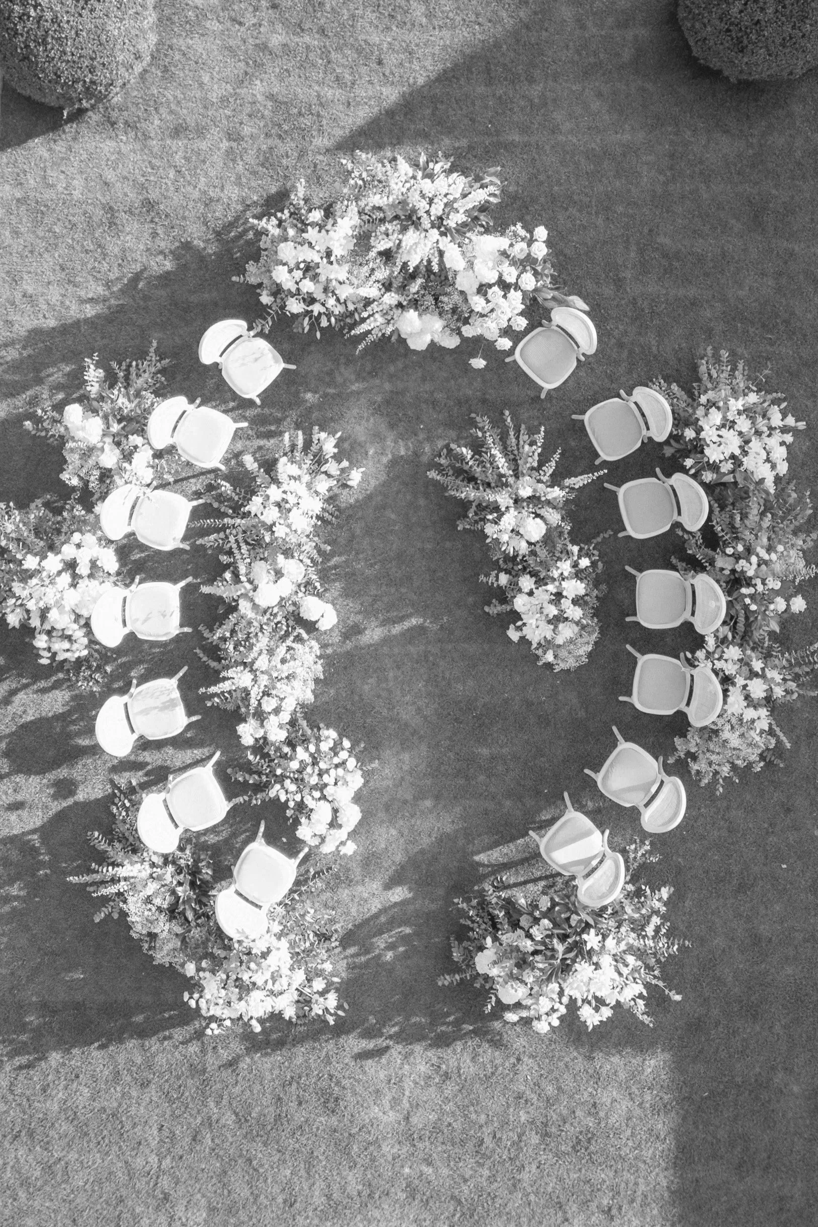 Aerial view of wedding ceremony setup with white chairs and floral arrangements on a grassy lawn.